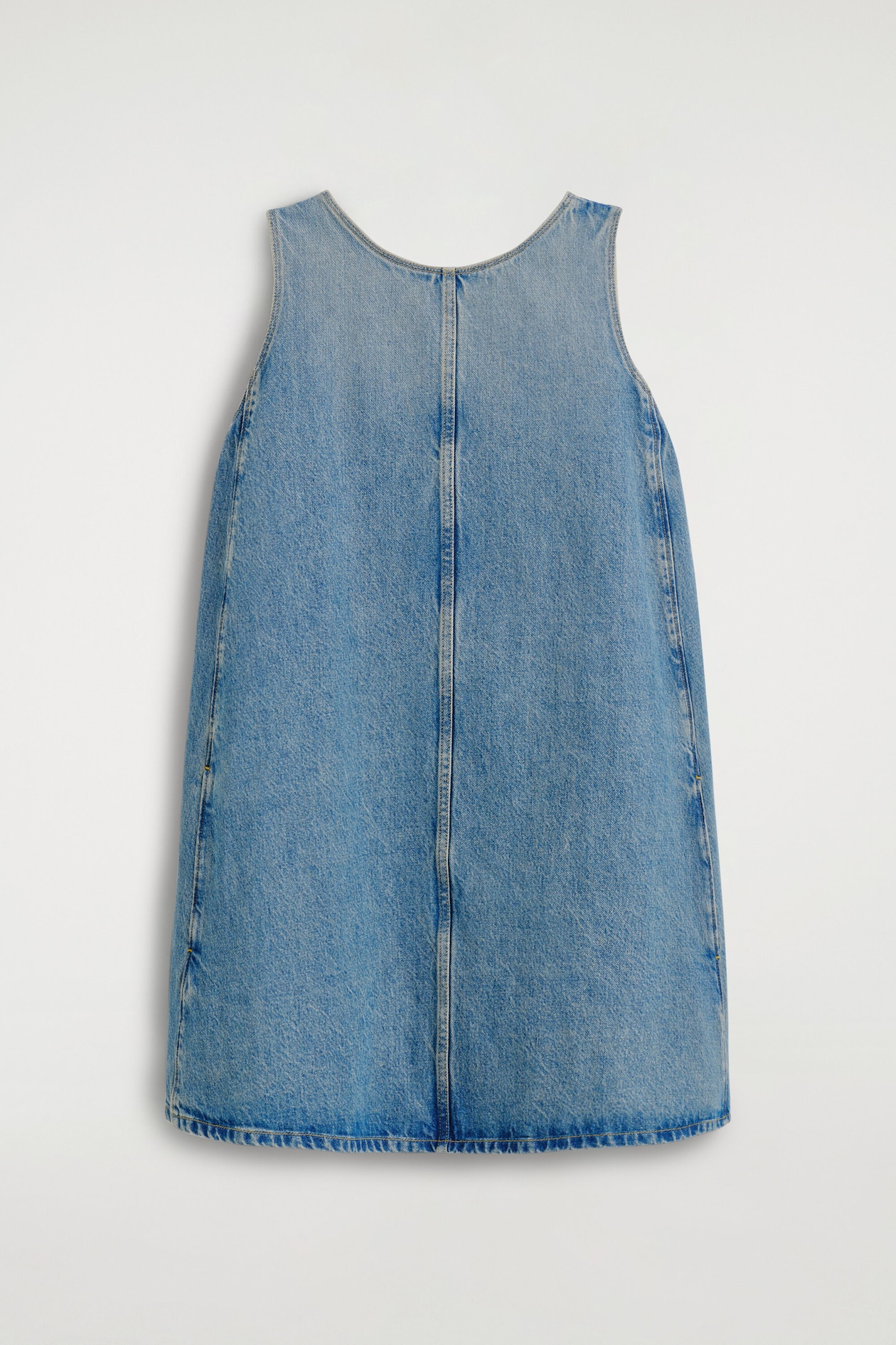 Un abito in denim blu senza maniche, con lavaggio da chiaro a medio, appeso e caratterizzato da girocollo, ampie spalline, cucitura centrale verticale e silhouette svasata a trapezio dal taglio pulito.