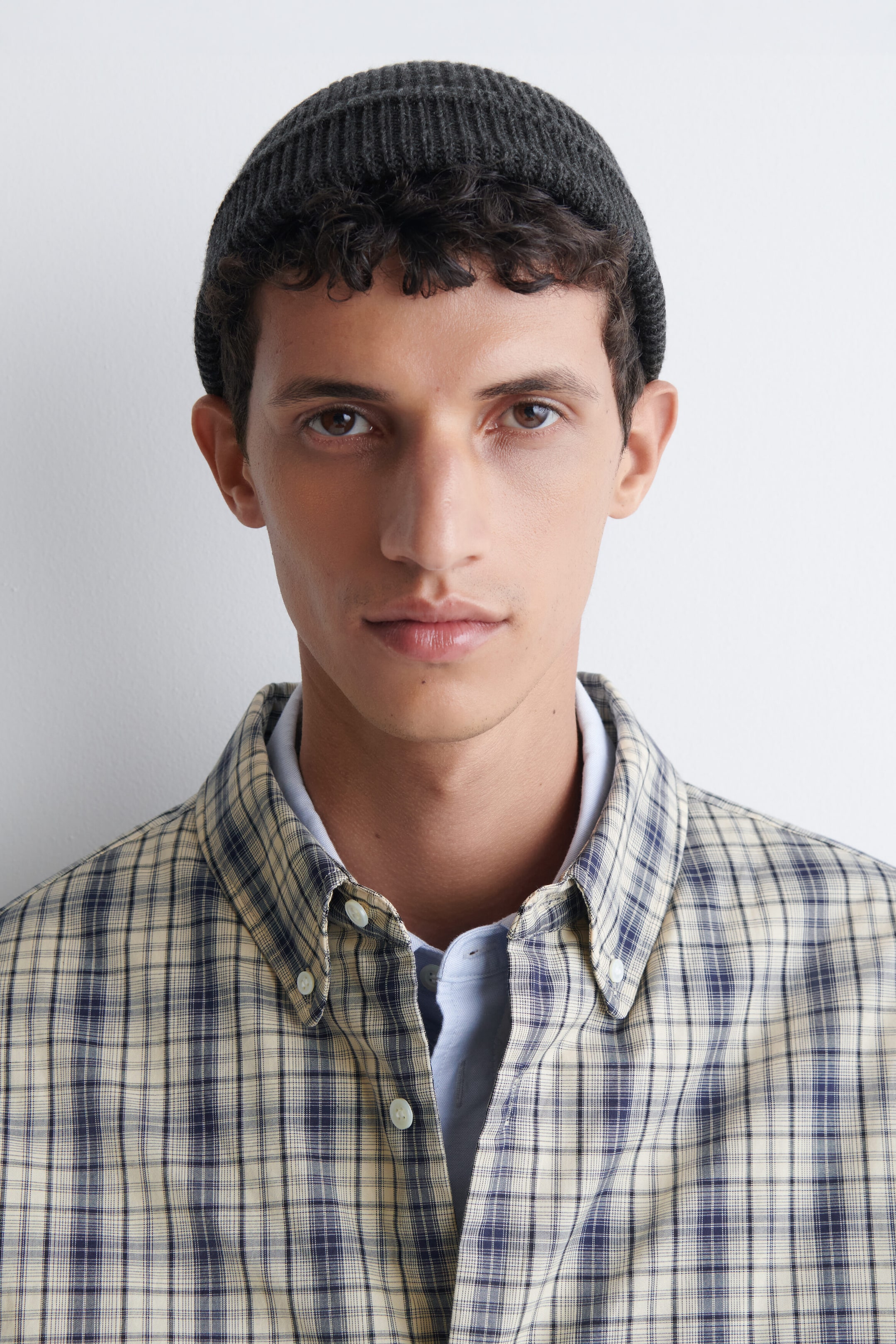 The model is wearing a dark gray ribbed wool-cotton fisherman beanie, fitted snugly on the head with the rolled cuff positioned above the ears.