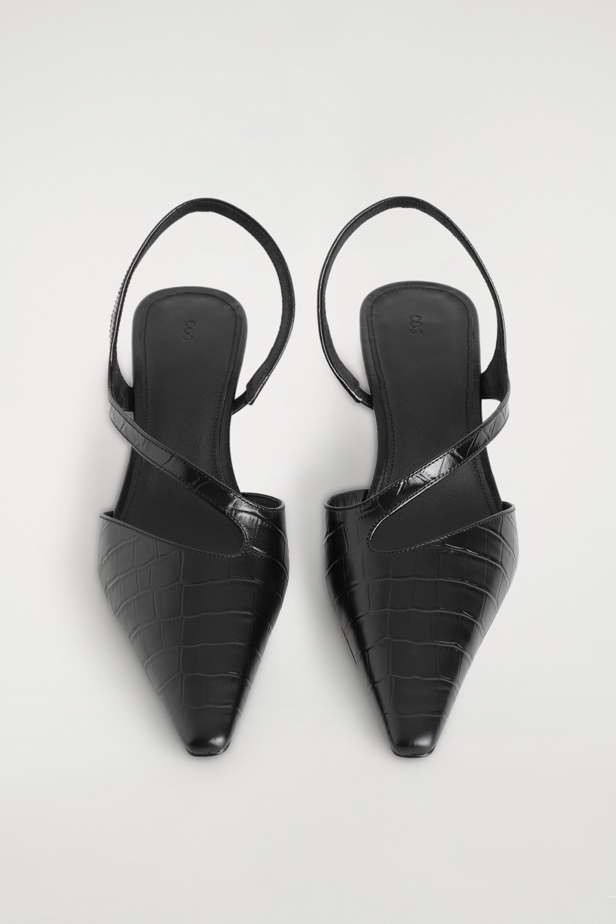 Croc-embossed leather slingback pumps feature a pointed-toe silhouette and a textured black crocodile-embossed finish, shown from the top to highlight their structure. The shoes showcase an asymmetric diagonal strap crossing over the instep and a matching slingback strap. Croc-embossed leather slingback pumps feature a pointed-toe silhouette and a textured black crocodile-embossed finish, shown from the top to highlight their structure. The shoes showcase an asymmetric diagonal strap crossing over the instep and a matching slingback strap.