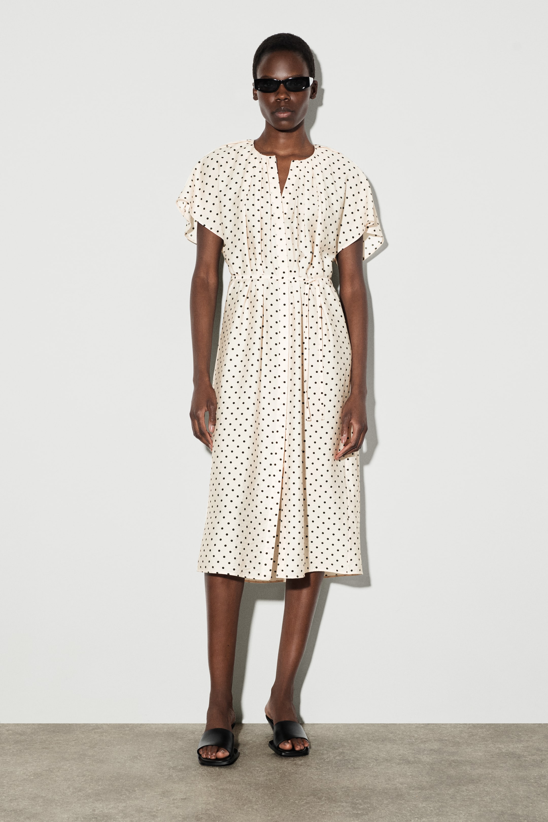 הצגת תמונה גדולה יותר: שמלת מידי בצבע קרם עם נקודות שחורות פונה קדימה. היא כוללת מחשוף בצורת V, שרוולים קצרים מתנפנפים ומותן מכווץ, ליצירת סילואט רפוי.
