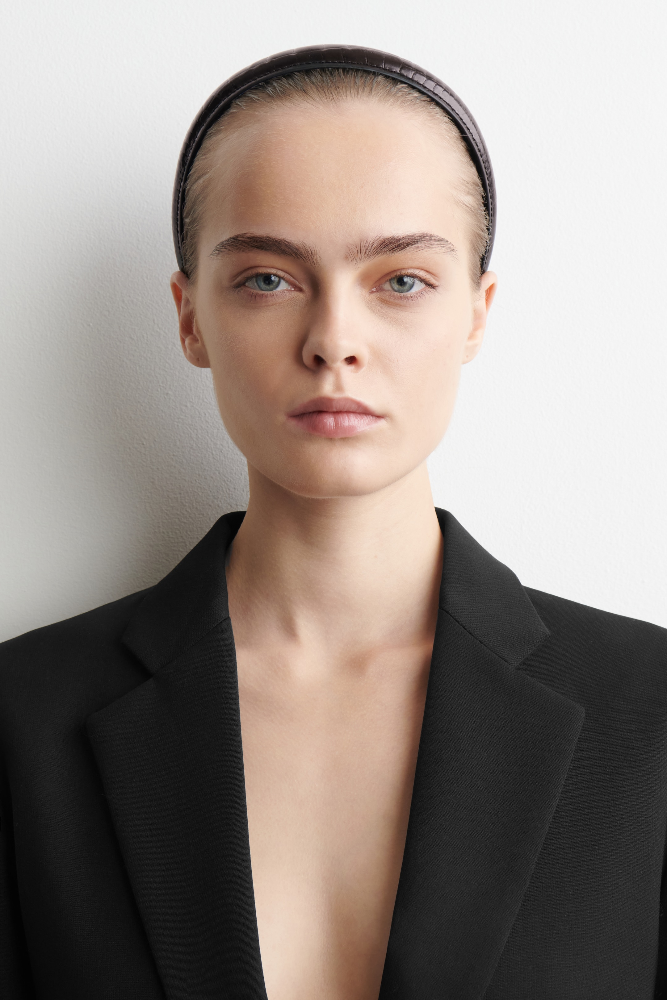 Ver imagen más grande: Se lleva un blazer negro, con solapas de muesca afiladas y hombros estructurados, presentado de frente. También se lleva una diadema oscura y grabada, visible en la parte superior de la cabeza.