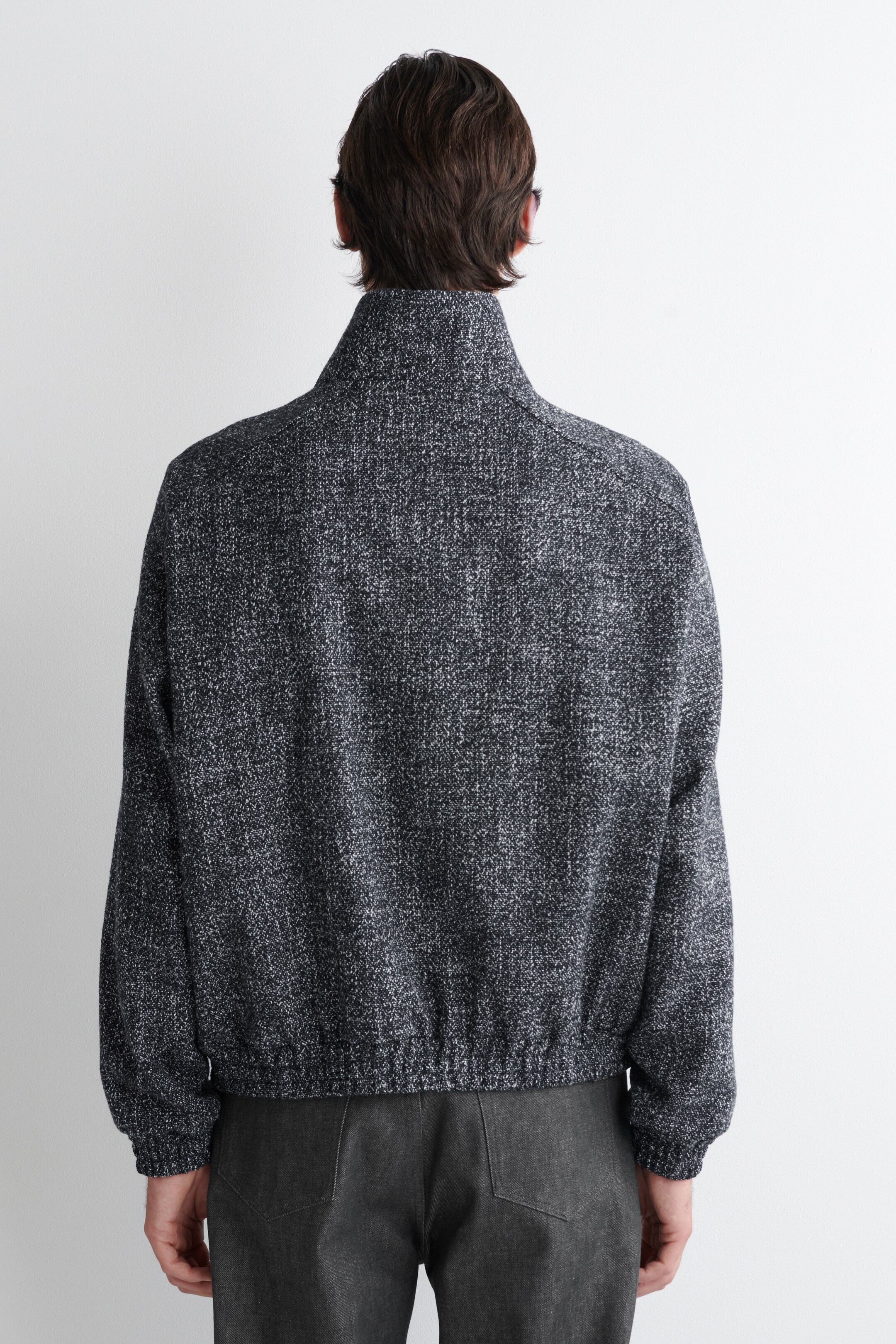 Grösseres Bild ansehen: Eine dunkelgraue gesprenkelte Jacke wird von hinten gezeigt. Sie besitzt einen Stehkragen, entspannte lange Ärmel mit elastischen Bündchen und einen elastischen Saum, der in der Taille zusammenzieht.