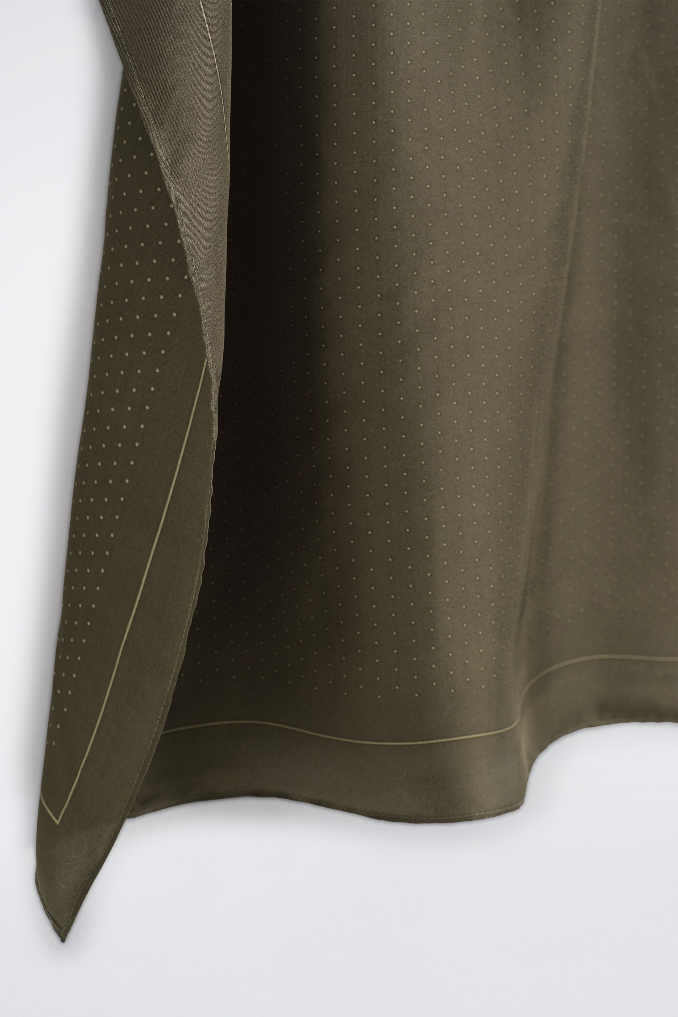 A polka-dot silk pocket square in olive green is draped vertically, displaying its smooth texture and soft folds. The pocket square features a pattern of tiny, light-colored polka dots and a thin, contrasting border line running parallel to its stitched edges. A polka-dot silk pocket square in olive green is draped vertically, displaying its smooth texture and soft folds. The pocket square features a pattern of tiny, light-colored polka dots and a thin, contrasting border line running parallel to its stitched edges.