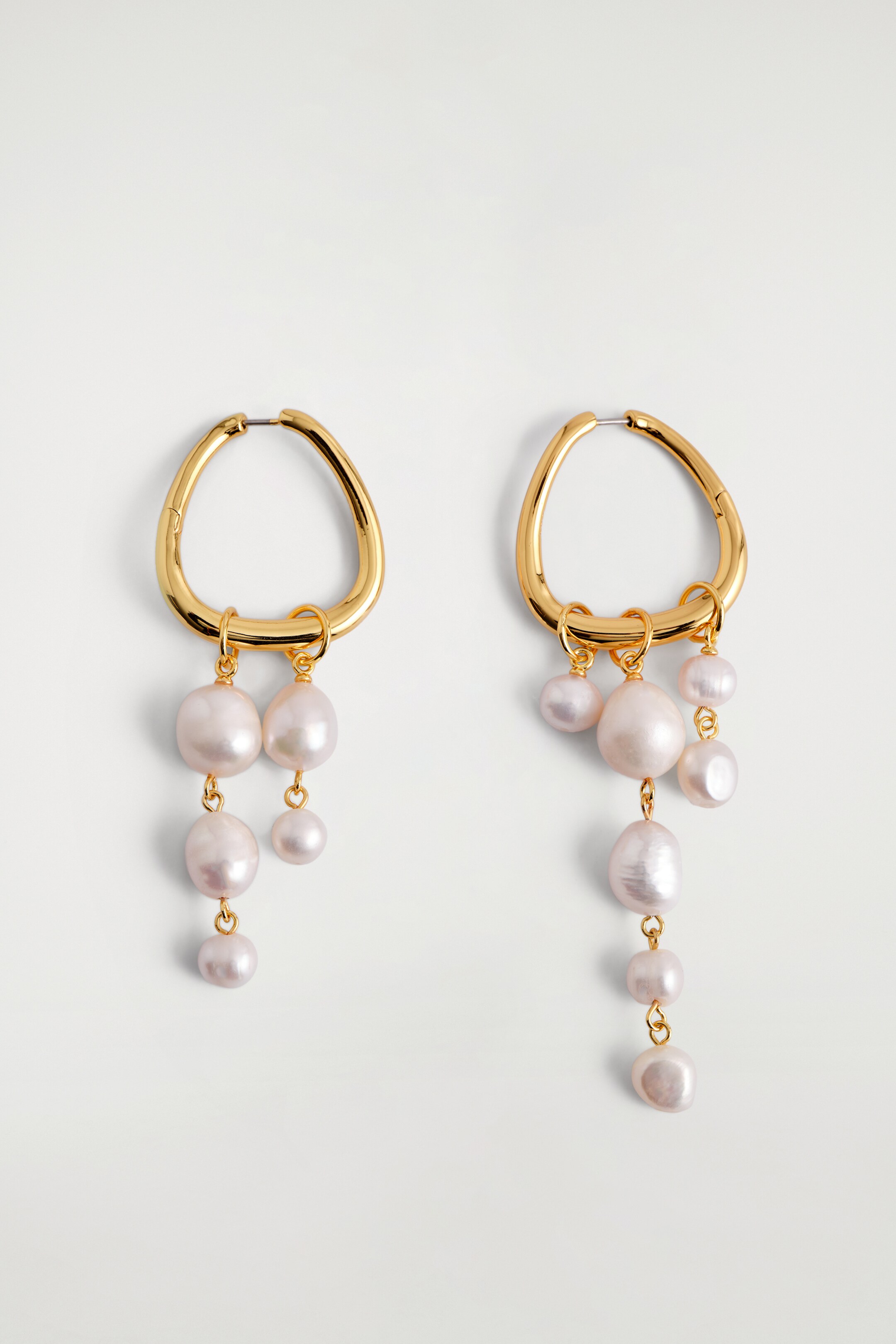 View larger image: A pair of gold-toned earrings are featuring irregular, slightly triangular hoop shapes at the TOP. Multiple light-toned, irregularly shaped baroque pearls of varying sizes are dangling from the bottom of each hoop, forming cascades.