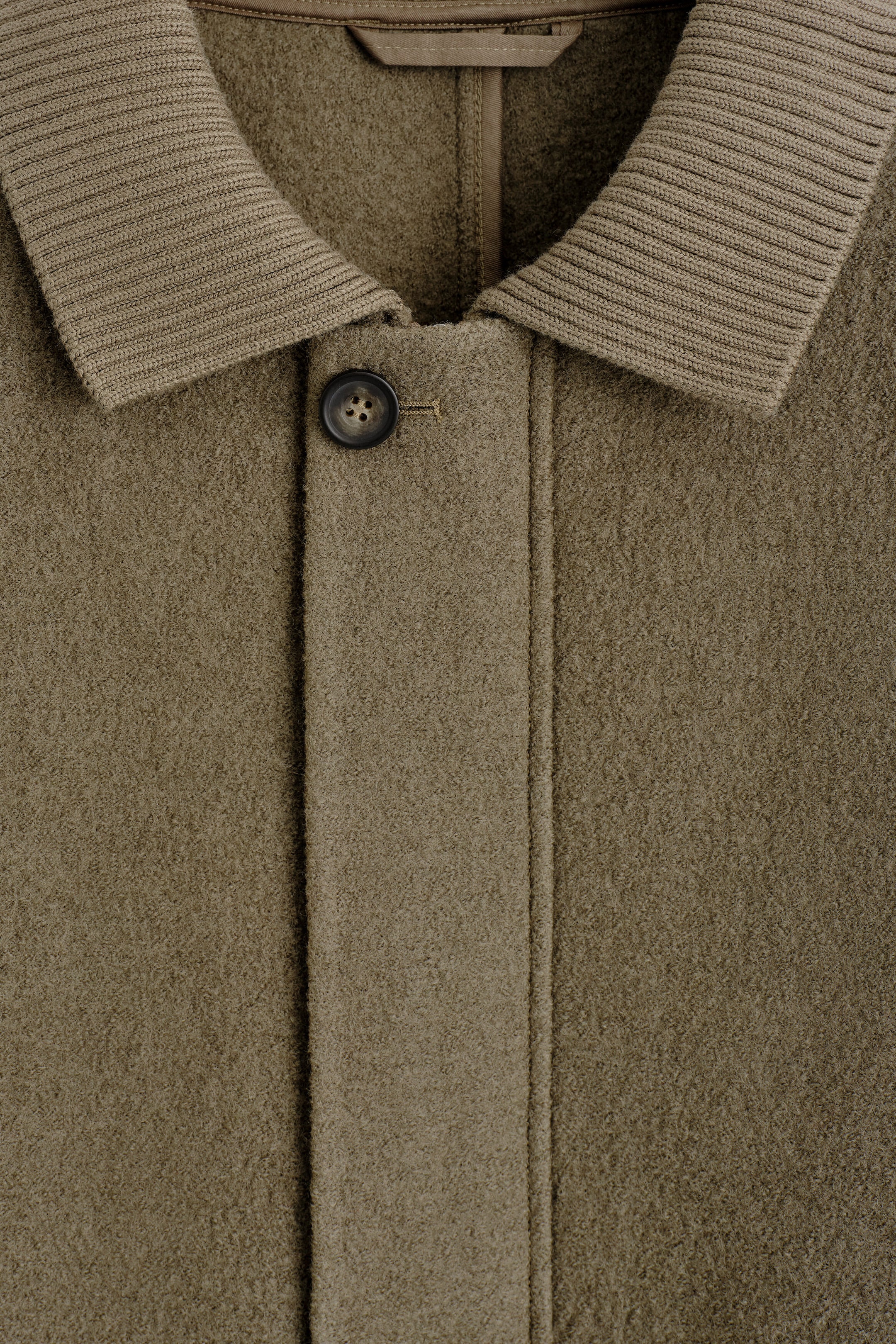 The ribbed-collar boiled-wool chore jacket is shown in a close-up front view, highlighting its textured olive-brown fabric and wide ribbed-knit collar. A single dark button secures the top of the concealed front placket beneath the open collar. The ribbed-collar boiled-wool chore jacket is shown in a close-up front view, highlighting its textured olive-brown fabric and wide ribbed-knit collar. A single dark button secures the top of the concealed front placket beneath the open collar.