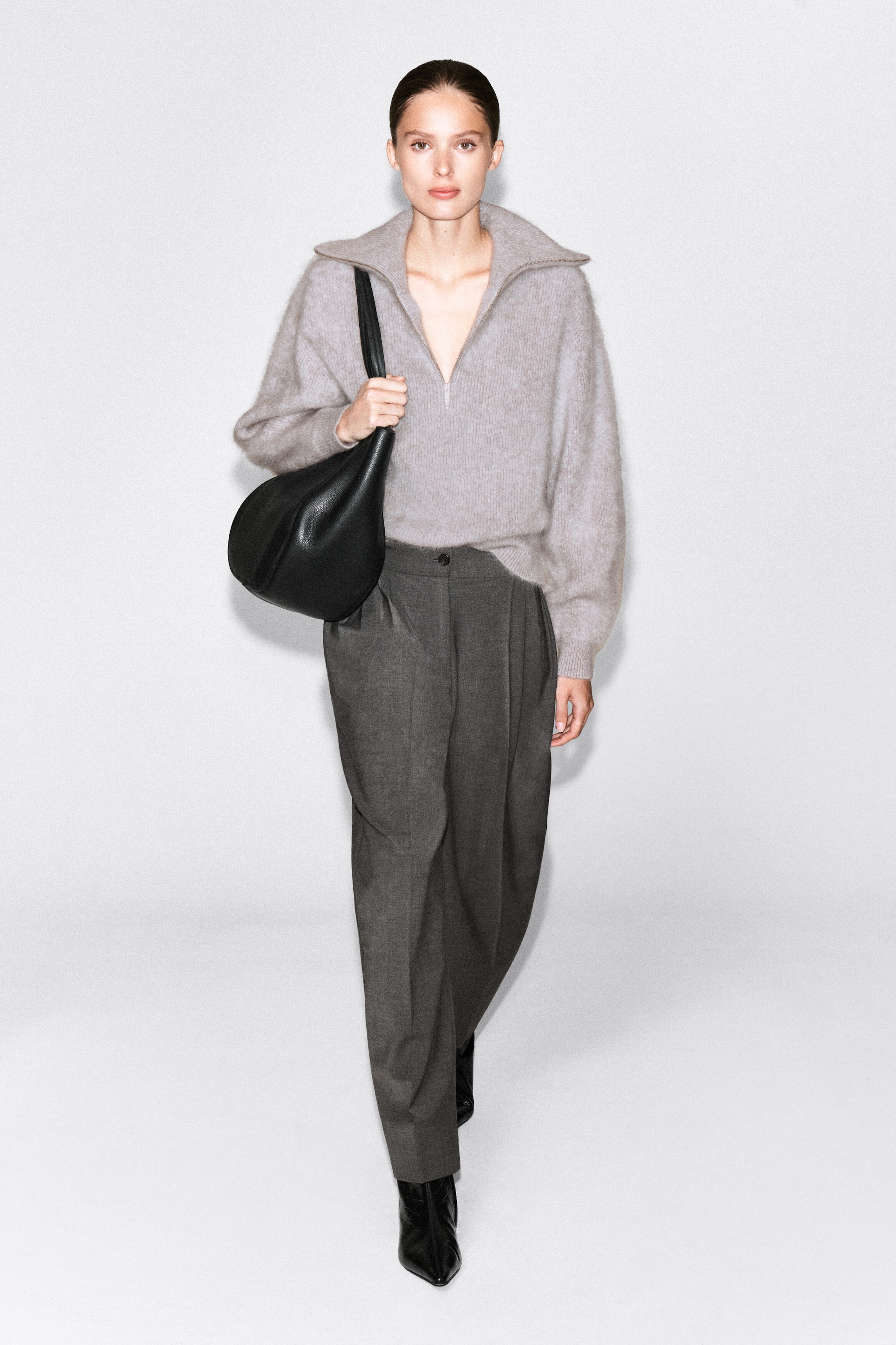 A light gray, brushed cashmere sweater featuring a half-zip funnel neckline and long sleeves is being worn by the model. The relaxed-fit sweater is styled with dark gray wide-leg trousers and a black leather shoulder bag. A light gray, brushed cashmere sweater featuring a half-zip funnel neckline and long sleeves is being worn by the model. The relaxed-fit sweater is styled with dark gray wide-leg trousers and a black leather shoulder bag.