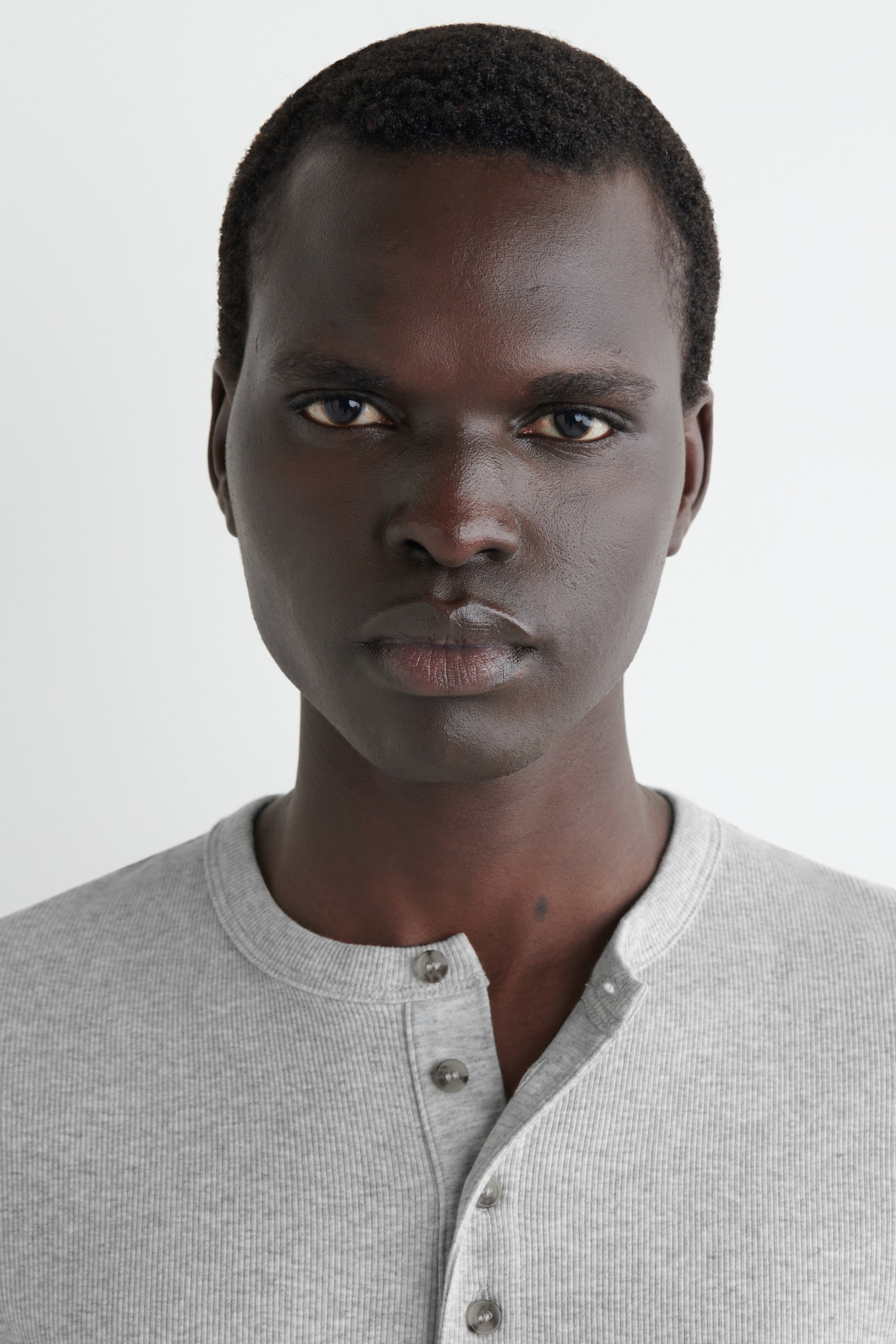 View larger image: A light grey ribbed knit Henley shirt is seen front-facing, featuring a round neckline and a partially unbuttoned four-button placket with mottled grey buttons.
