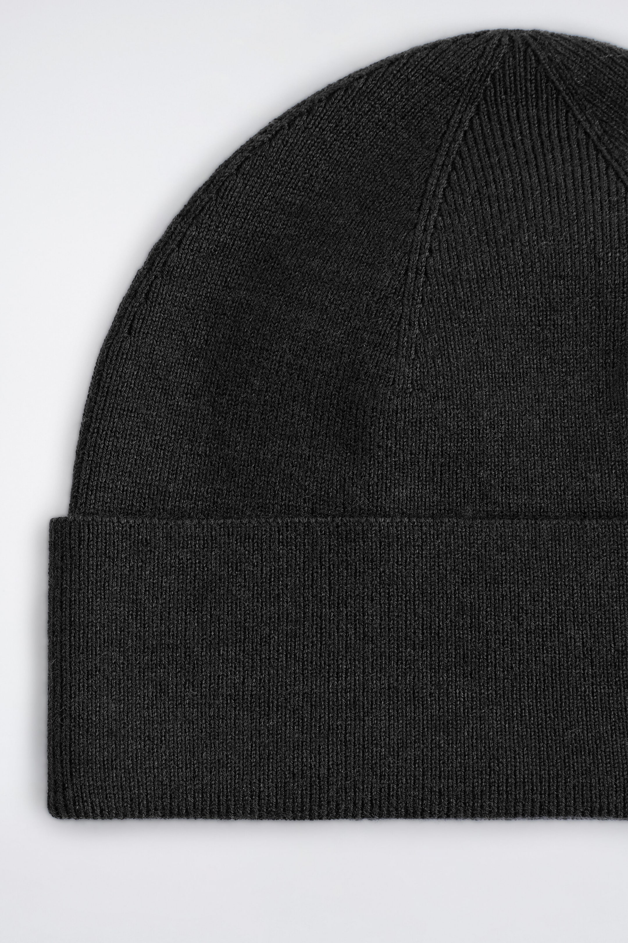 A close-up view showcases a dark gray knitted beanie, highlighting its fine-ribbed fold-up brim and seamless knit construction on the crown.