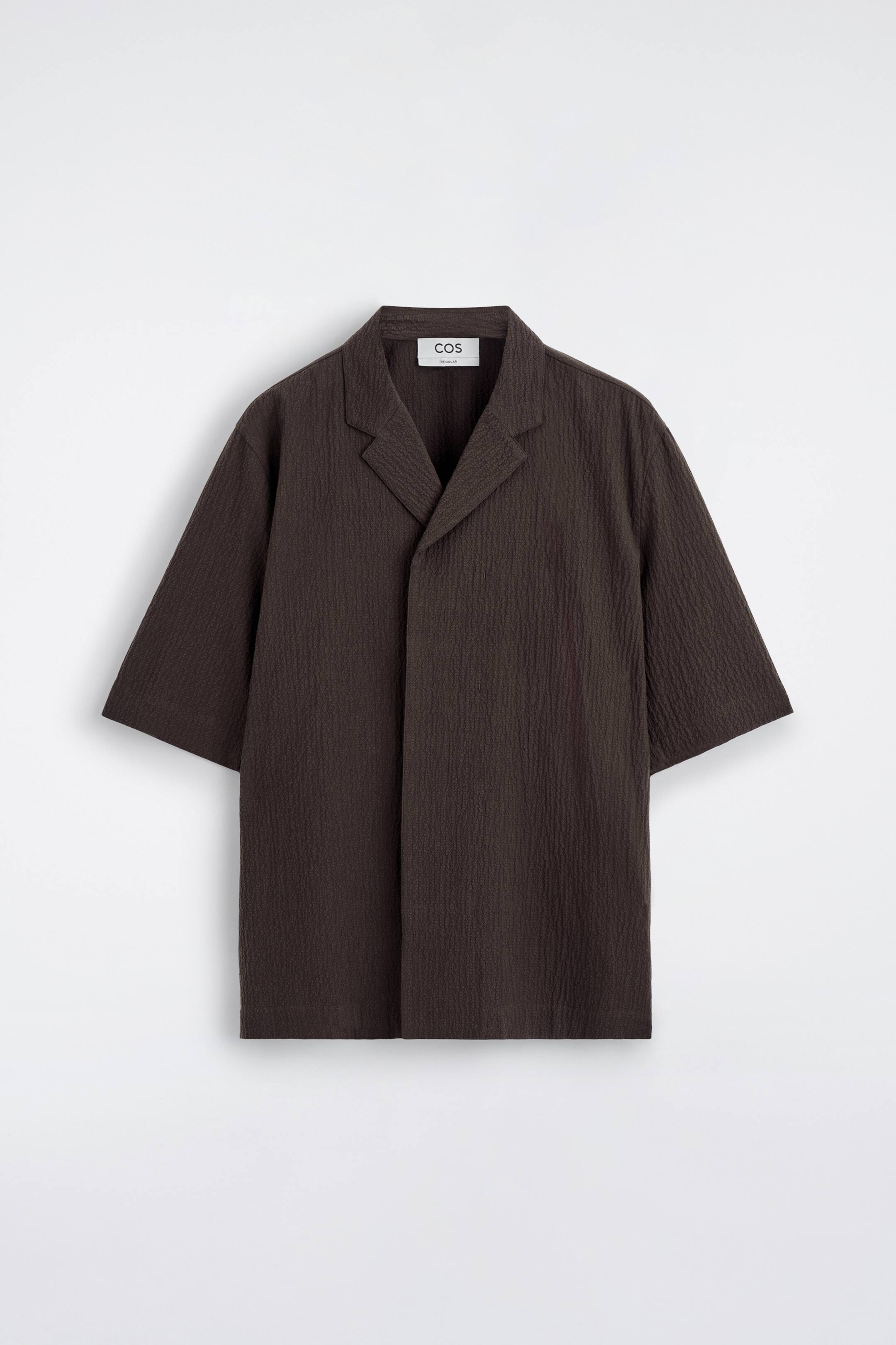 Visualizza immagine più grande: Una camicia da resort marrone scuro presenta una vestibilità rilassata, tessuto seersucker strutturato, colletto aperto e maniche corte.