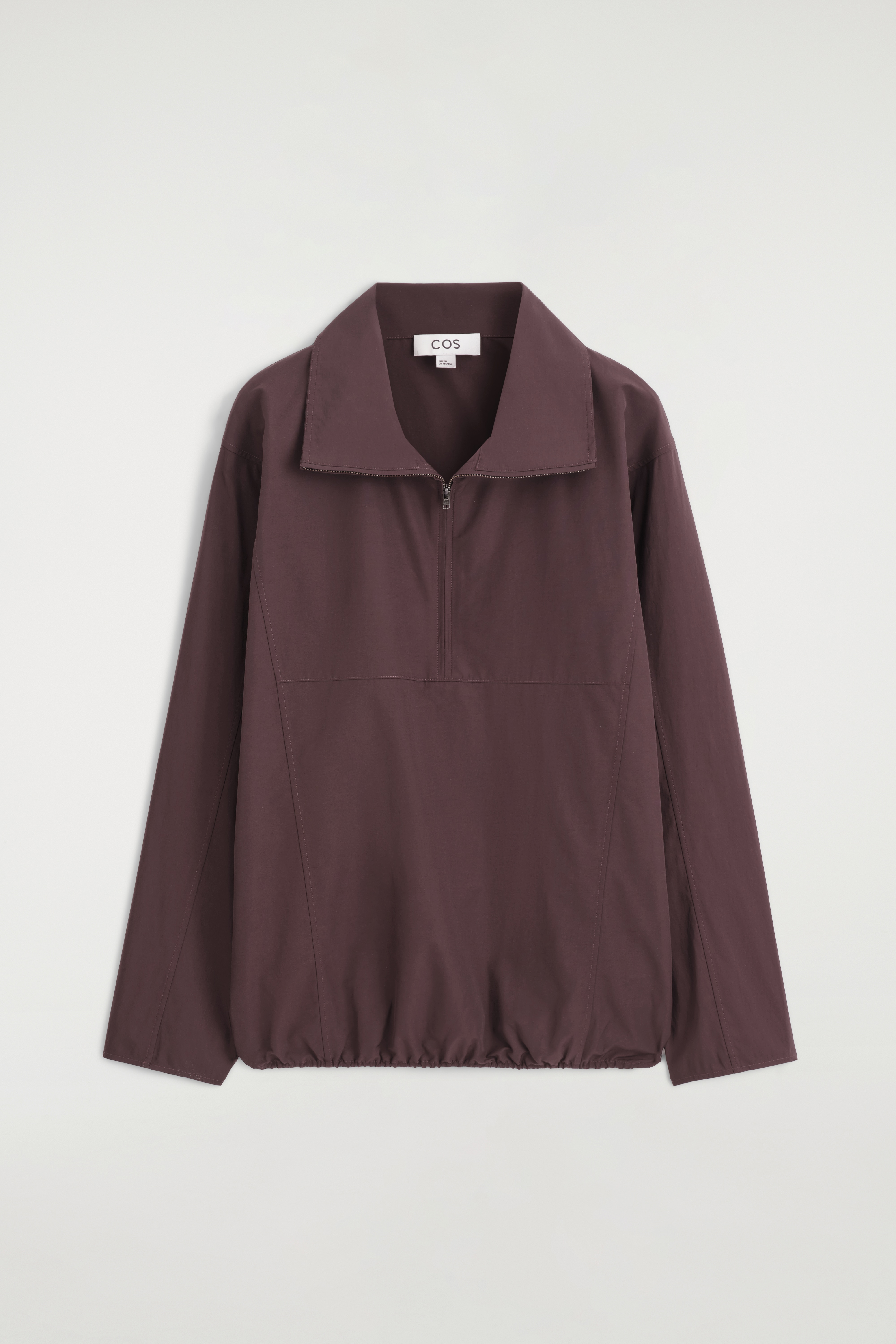 Un pull-shirt Ã  demi-zip en prune foncÃ© est prÃ©sentÃ© de face, avec un col montant haut et une fermeture Ã©clair argentÃ©e, des manches longues et un ourlet froncÃ© Ã  cordon de serrage.