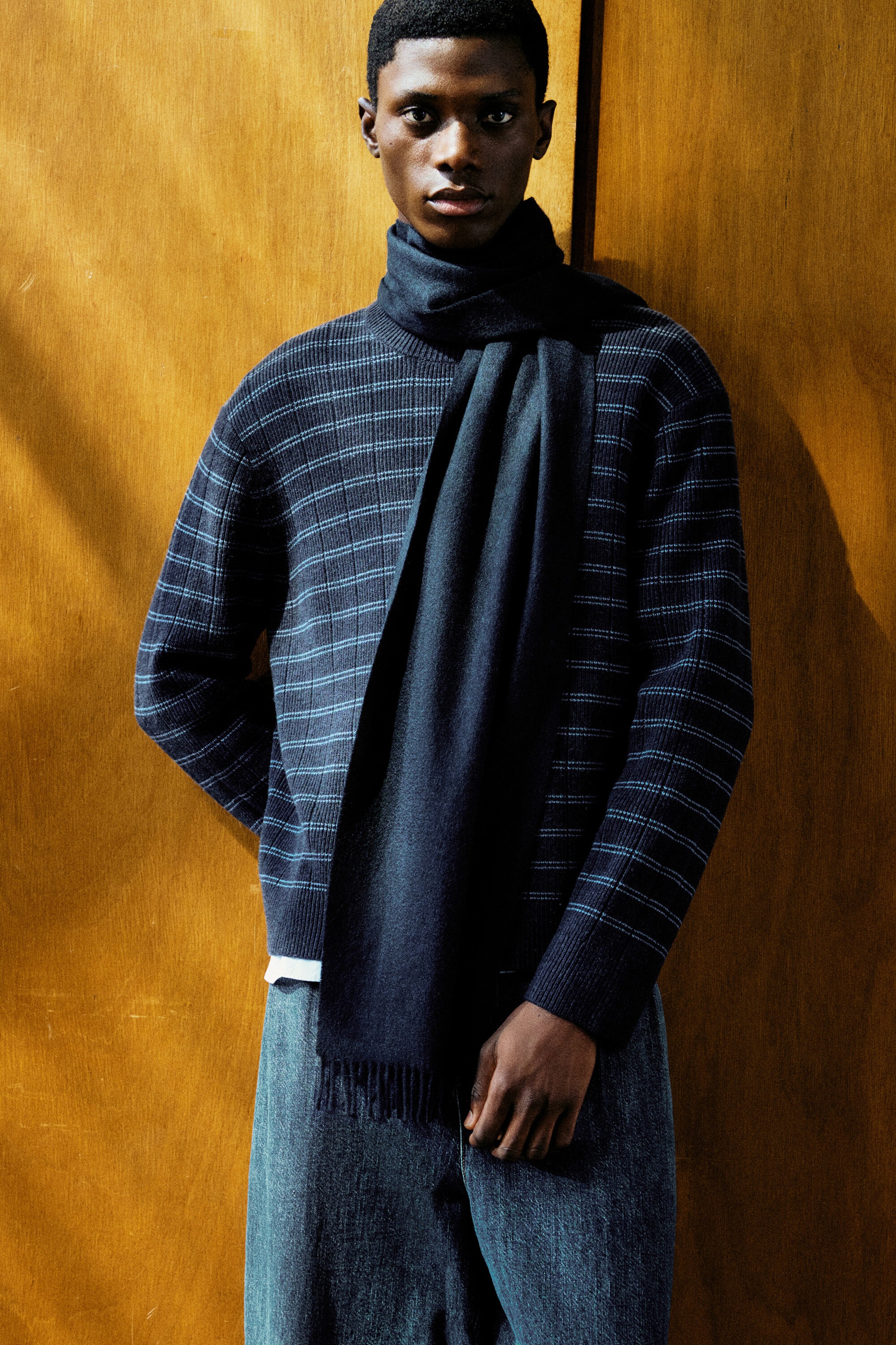 A model is facing forward, wearing a dark navy striped merino-cashmere jumper featuring thin, horizontal light blue stripes, a crew neck, and ribbed cuffs. A solid dark navy cashmere scarf is wrapped around the neck, draping down the front and displaying a fringed hem. A model is facing forward, wearing a dark navy striped merino-cashmere jumper featuring thin, horizontal light blue stripes, a crew neck, and ribbed cuffs. A solid dark navy cashmere scarf is wrapped around the neck, draping down the front and displaying a fringed hem.
