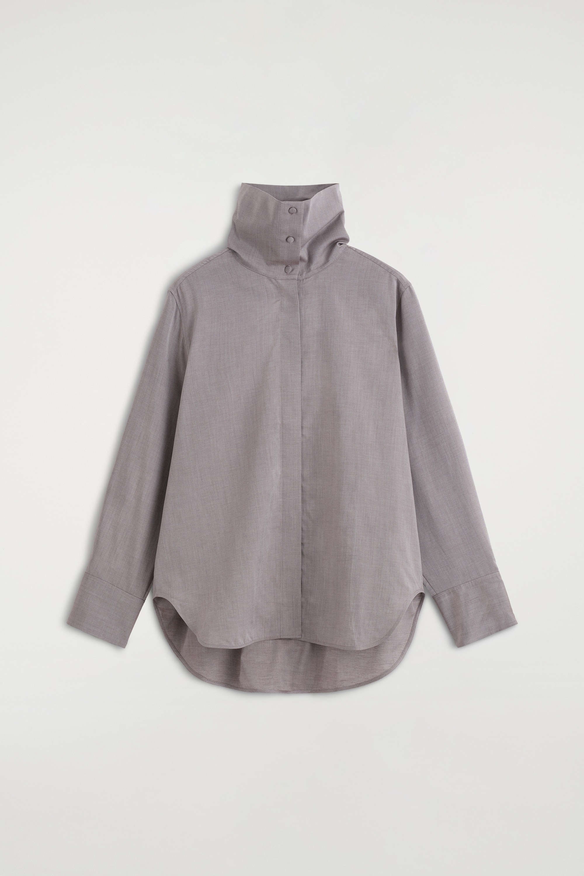 Una camicia grigia a maniche lunghe con collo alto drappeggiato a cappuccio e dettagli con bottoni Ã¨ indossata dalla modella, infilata in pantaloni neri con cintura. La camicia ha una leggera lucentezza ed Ã¨ abbinata con le maniche risvoltate fino ai gomiti.