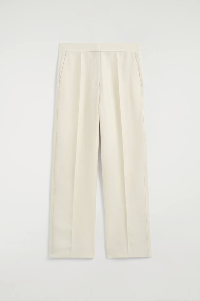 These cream straight-leg trousers are showcased from the front, featuring a tailored waistband, side seam pockets, and visible creases running down the front of each leg. - 1