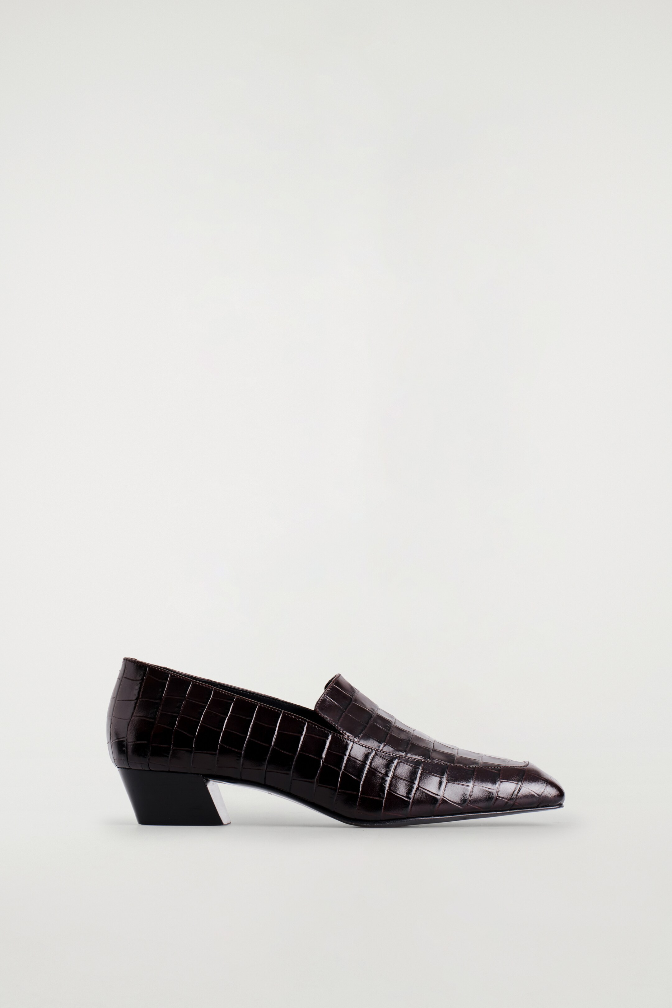 Größeres Bild ansehen: Ein dunkelbrauner Loafer zeigt nach rechts, mit einer Krokodil-Effekt-Textur, einer spitzen Zehe und einem eckigen Absatz mit einem silbernen Innendetail.