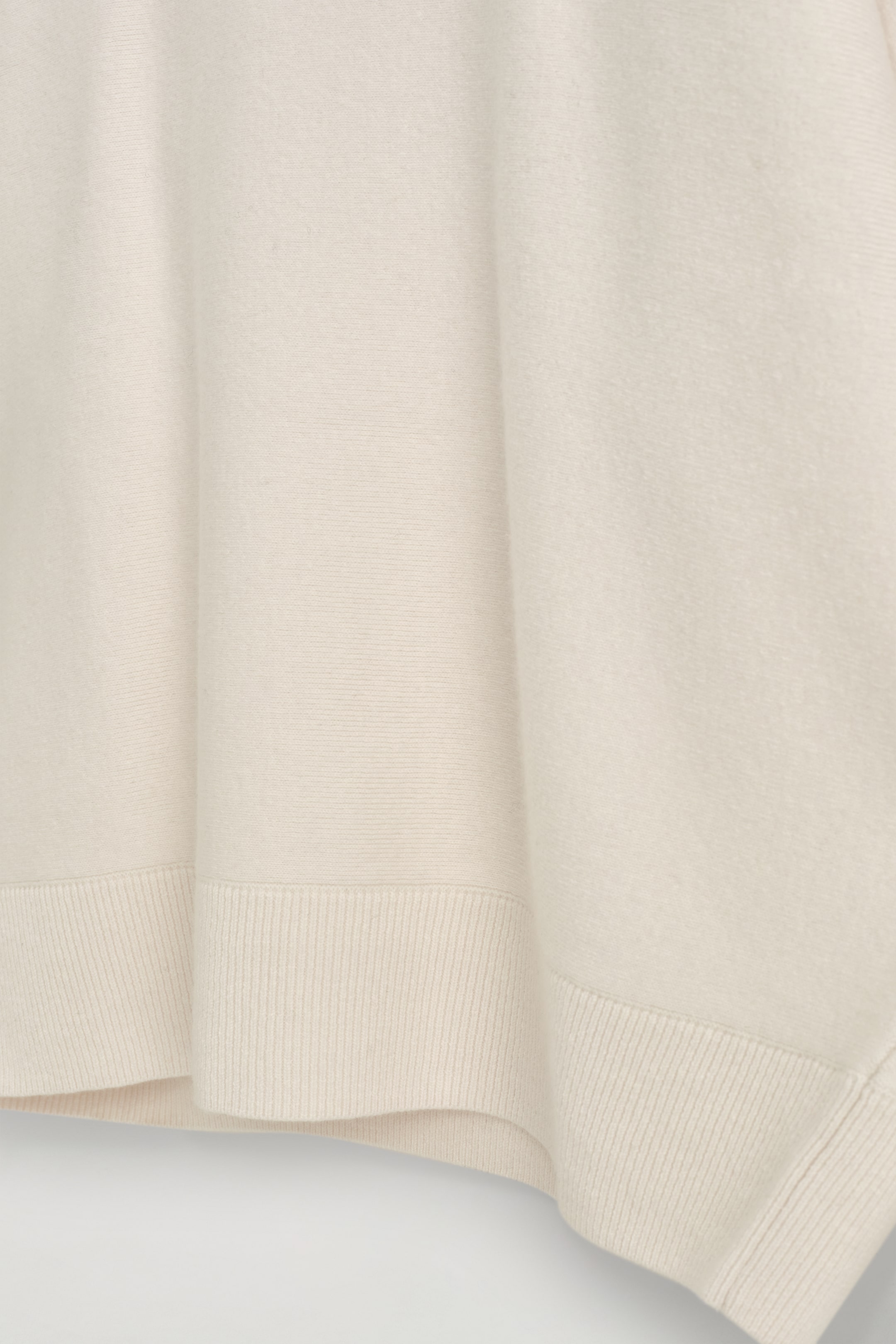 Visualizza immagine più grande: Un maglione lavorato a maglia di colore crema presenta una texture di tessuto morbida e drappeggiata. Il suo corpo principale mostra una maglia fine e liscia, che si trasforma in un orlo a coste distinto nella parte inferiore.