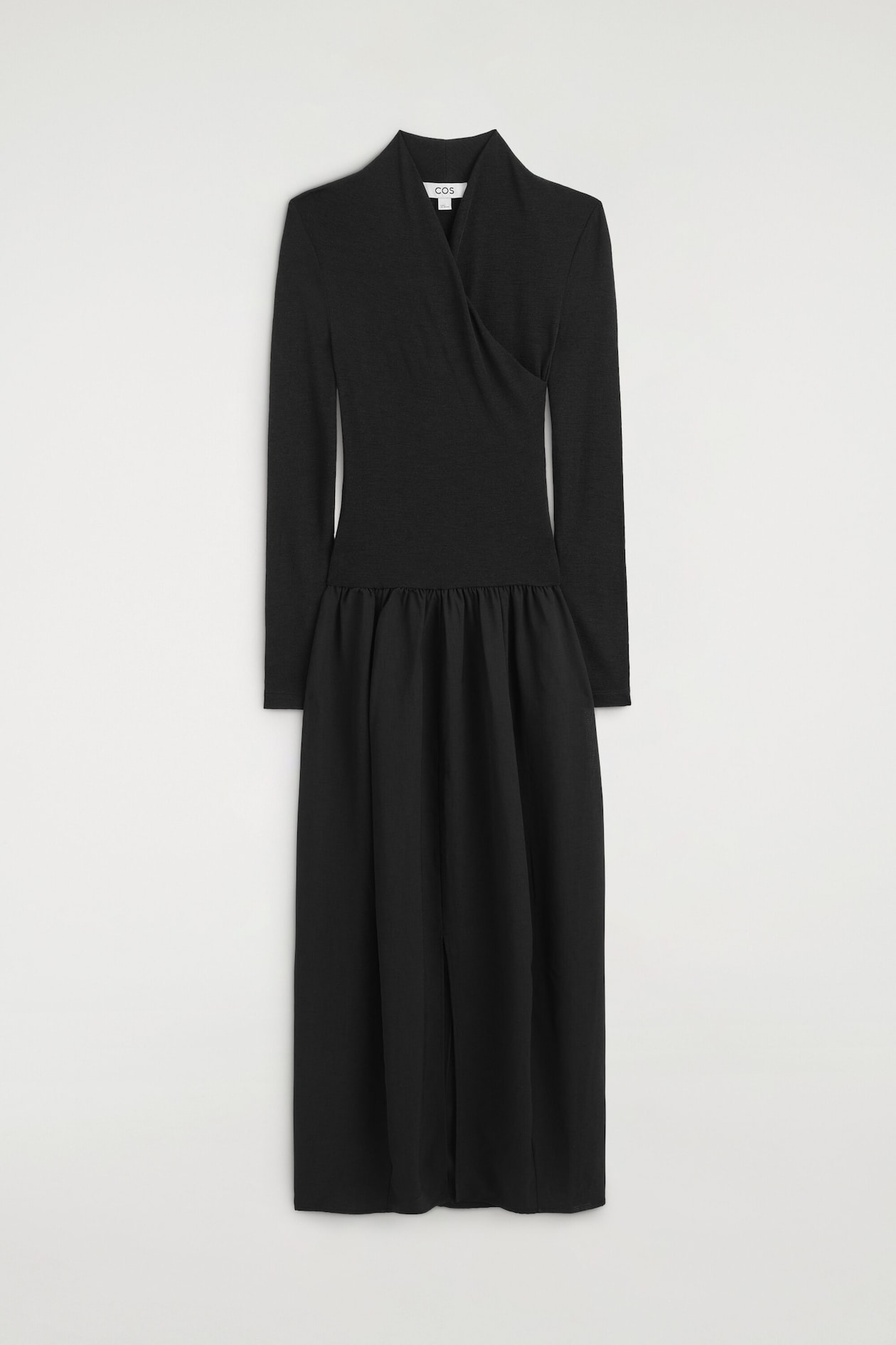 The black contrast-panel wrap-over dress is hanging flat in a front view, showcasing a fitted, long-sleeved bodice with a high crossover neckline. The dress transitions at the dropped waist into a gathered, contrasting-fabric midi skirt that drapes down with a centre-front slit.