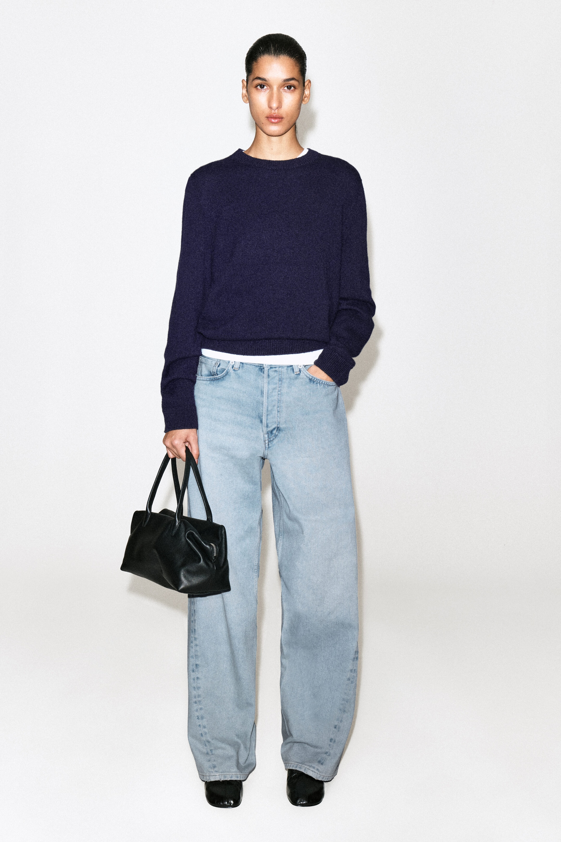 The Facade straight-leg jeans are worn facing forward, showcasing a light blue wash, a relaxed straight-leg silhouette, and classic five-pocket construction. The jeans fall loosely over black shoes, with a navy crew-neck jumper layered over a white T-shirt framing the mid-rise waistband.
