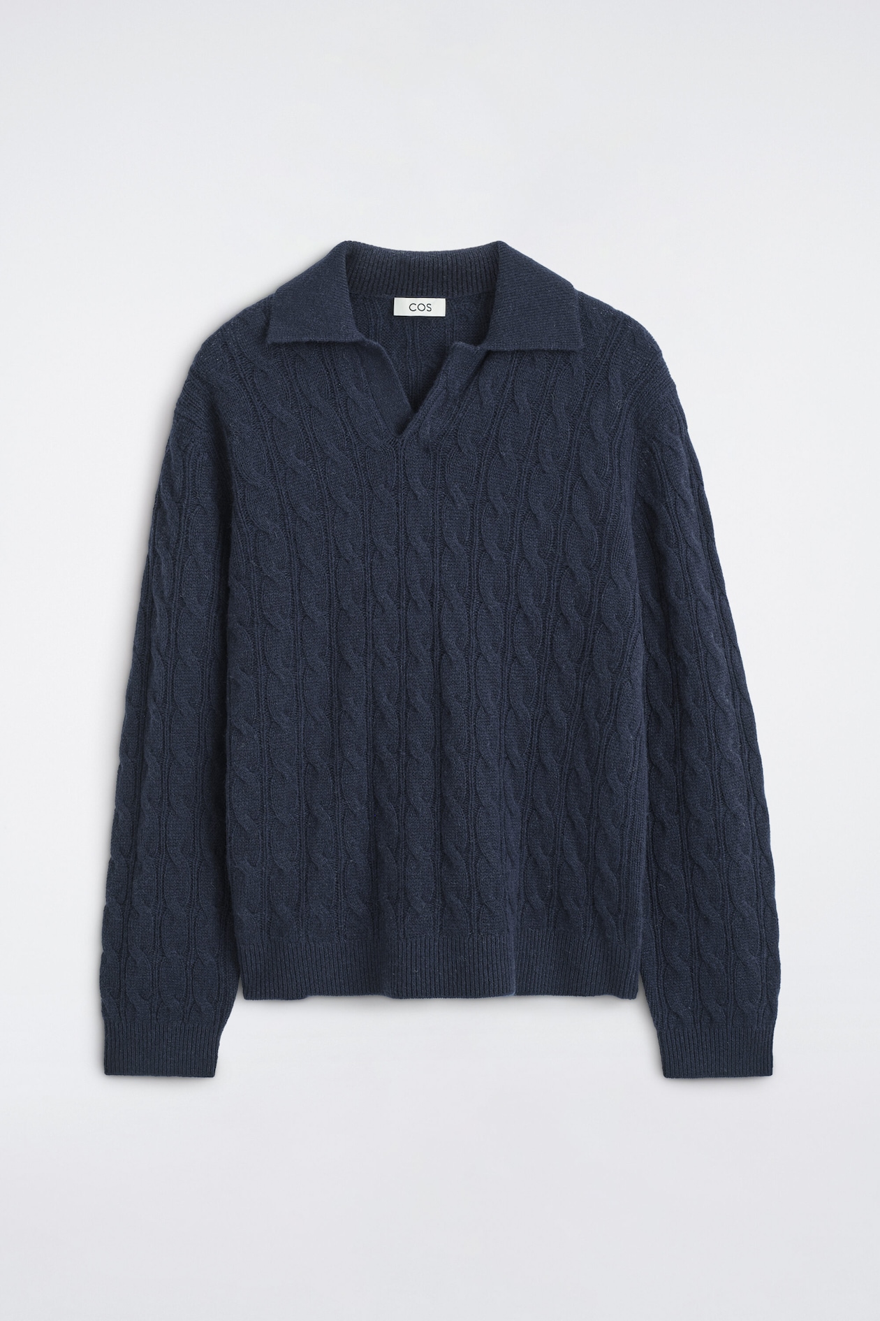 A navy blue cable-knit cashmere polo sweater is shown from the front, featuring an open, buttonless polo collar and a classic V-neck. The long-sleeved garment features an all-over vertical cable-knit pattern with ribbed detailing at the cuffs and hem.