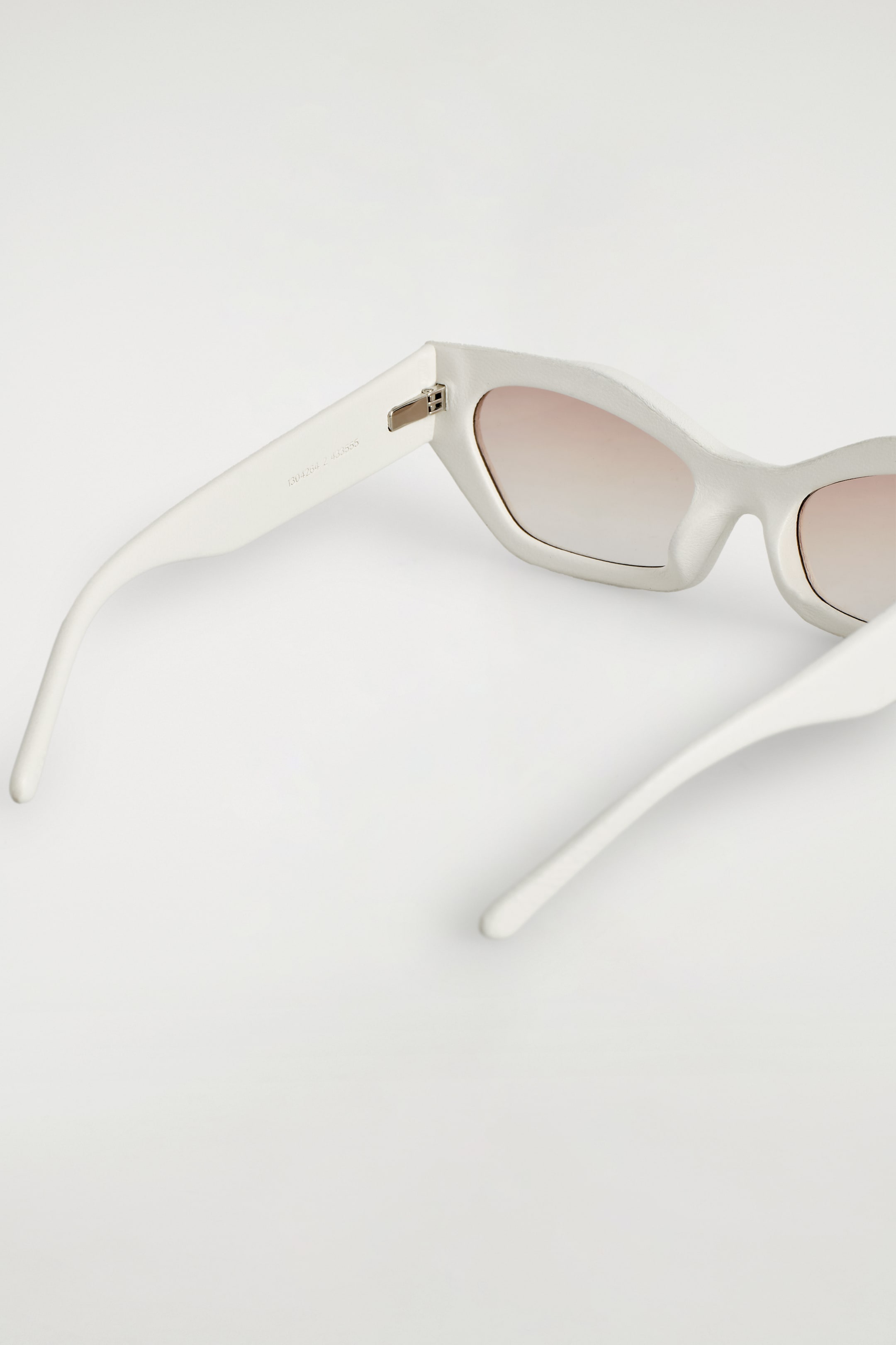 View larger image: Angular cat-eye sunglasses are presenting their back view, featuring a textured white frame and gradient lenses. Silver-toned metal hinges are connecting the frame to the tapered temples.