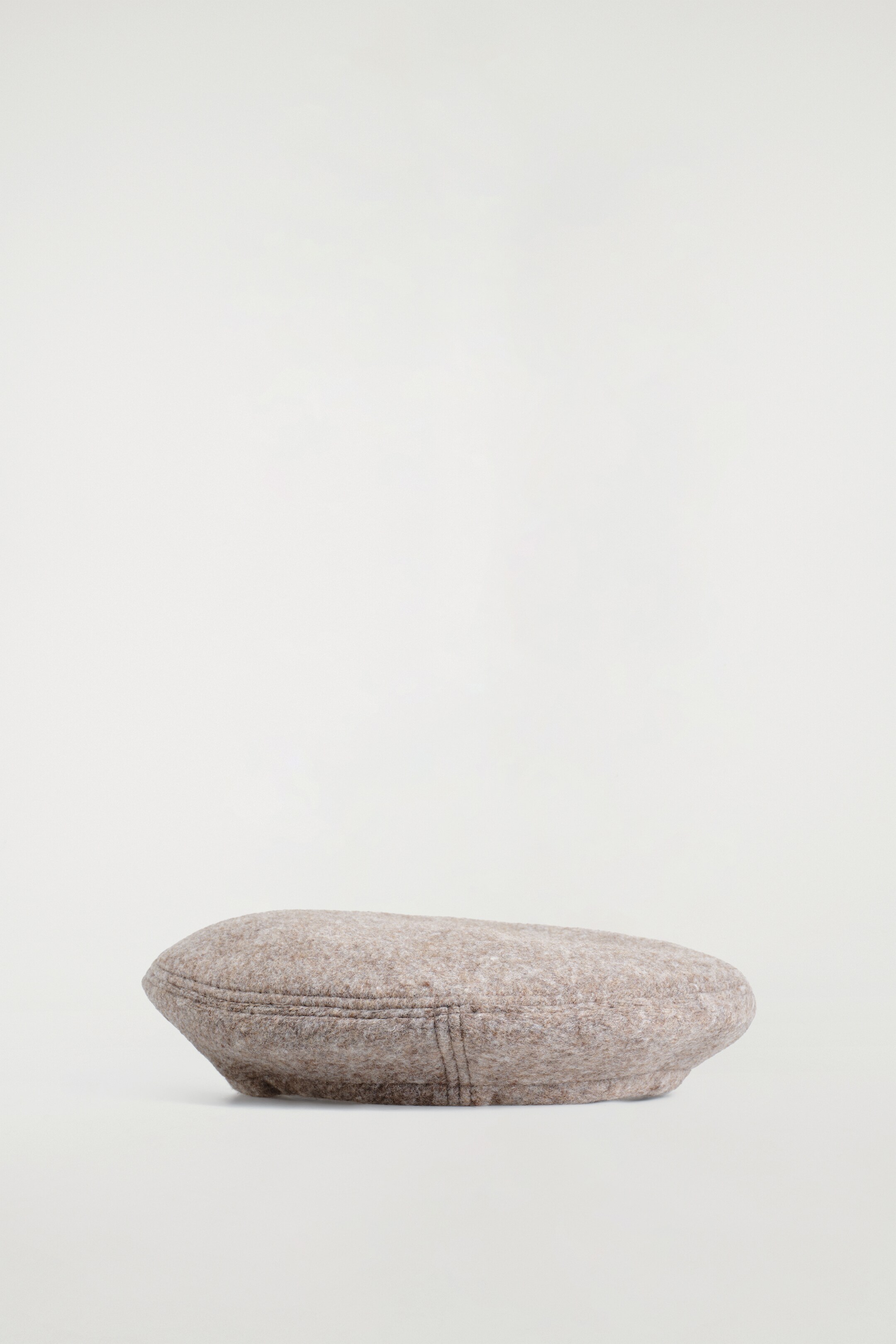 Agrandir l'image: Un béret dans une teinte beige-mélange repose à plat, vu de côté. Il affiche une texture tactile chinée et des lignes de couture visibles formant des panneaux sur sa couronne arrondie et le long du bord.