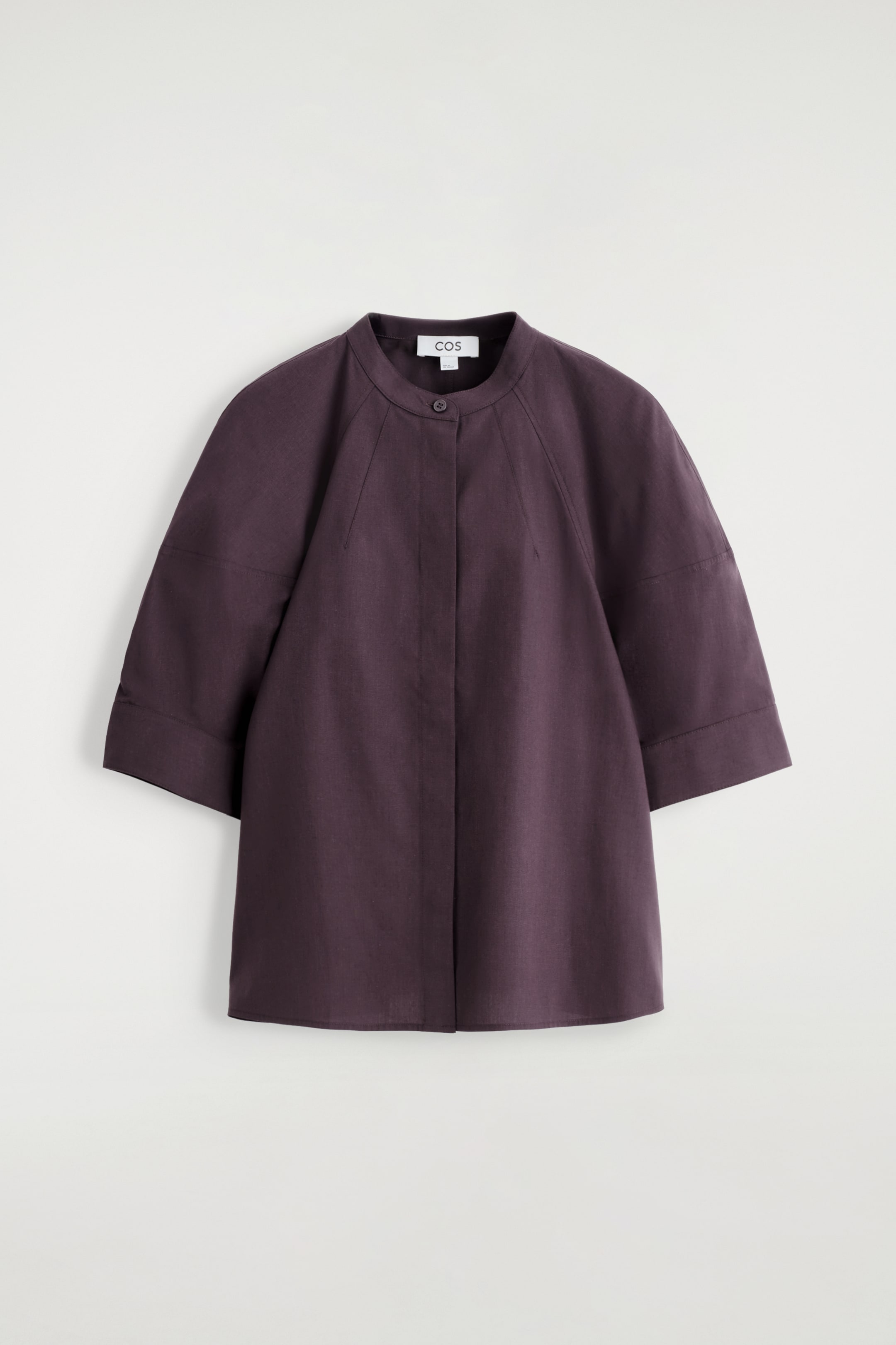 Visualizza immagine più grande: Una blusa color prugna scuro viene presentata dal davanti, caratterizzata da un colletto rotondo alla coreana e una chiusura con un solo bottone visibile. Ha maniche raglan voluminose a 3/4 con polsini larghi e una silhouette leggermente svasata, il tutto realizzato in un tessuto leggero.