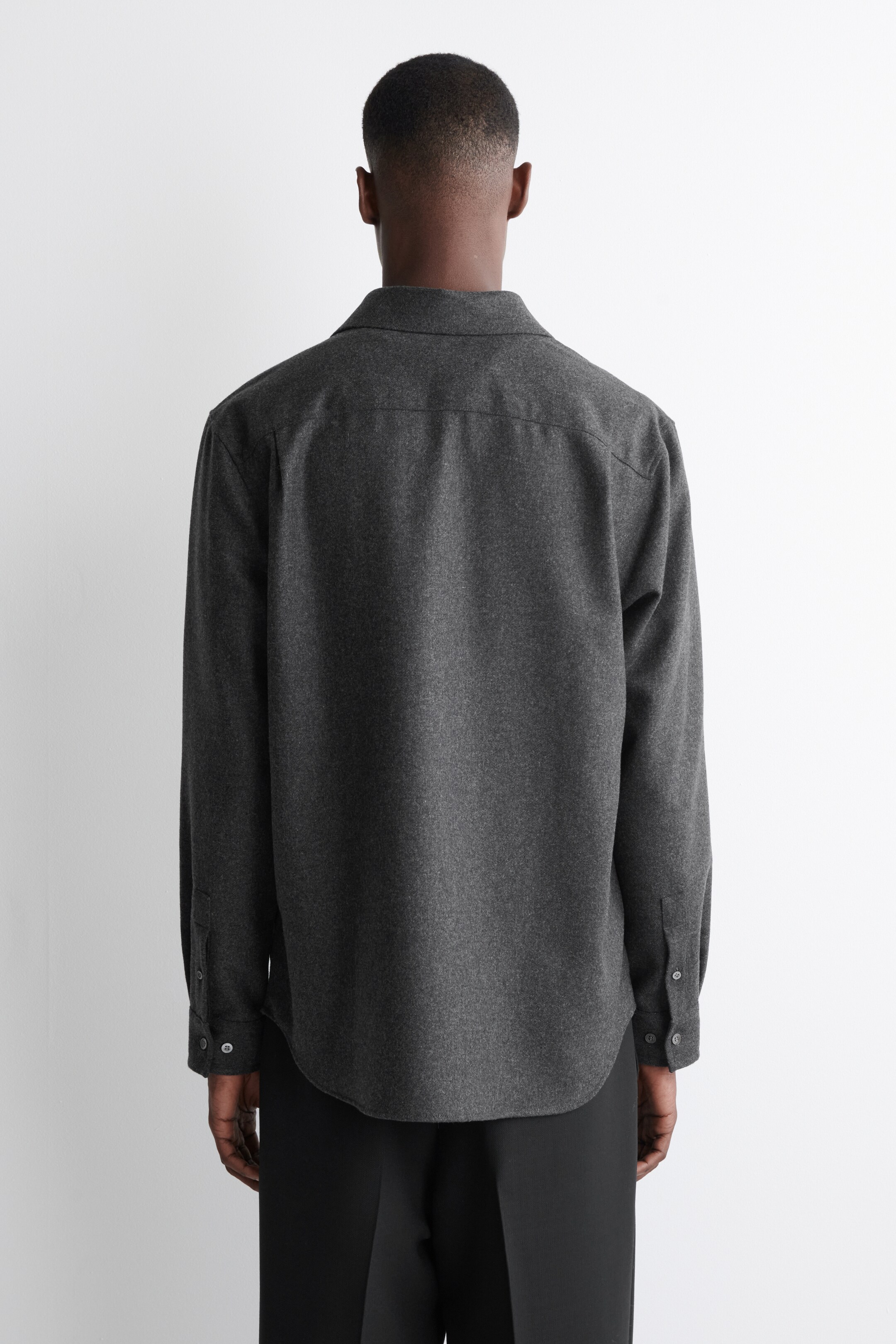Visualizza immagine più grande: Una camicia a maniche lunghe di colore grigio scuro, realizzata in un tessuto con una texture sottile e vista dal retro, presenta un colletto classico, un giogo posteriore e polsini con due bottoni visibili. La camicia presenta una vestibilità rilassata e un orlo arrotondato.