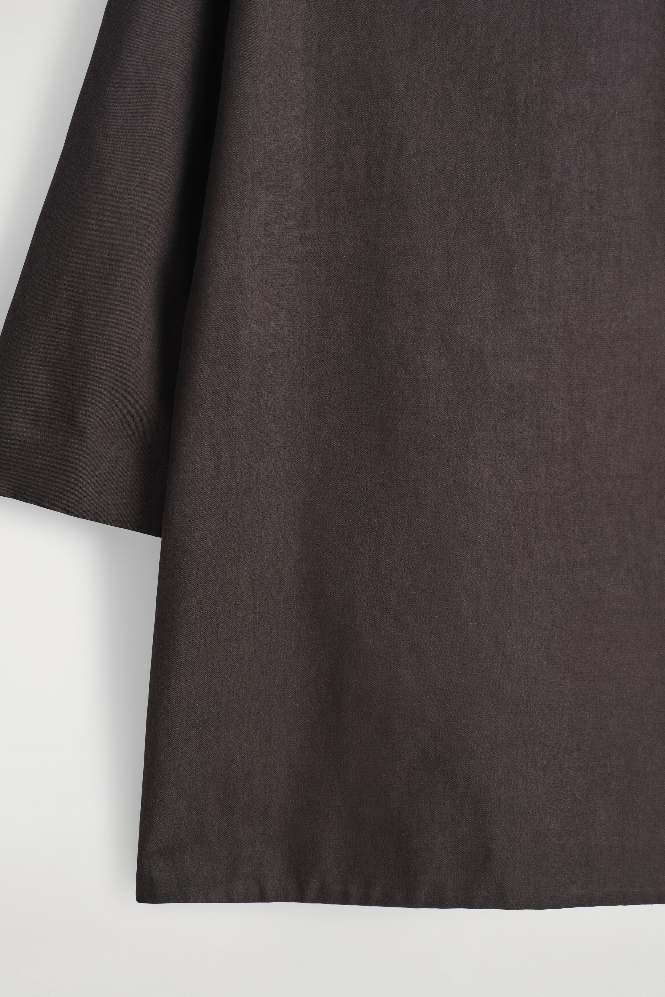 Größeres Bild anzeigen: Ein A-Linien-Kleid aus einem dunklen, strukturierten Leinen-Mix wird gezeigt, mit einem weiten, gekürzten Ärmel auf der linken Seite und einem geraden Saum am unteren Ende.