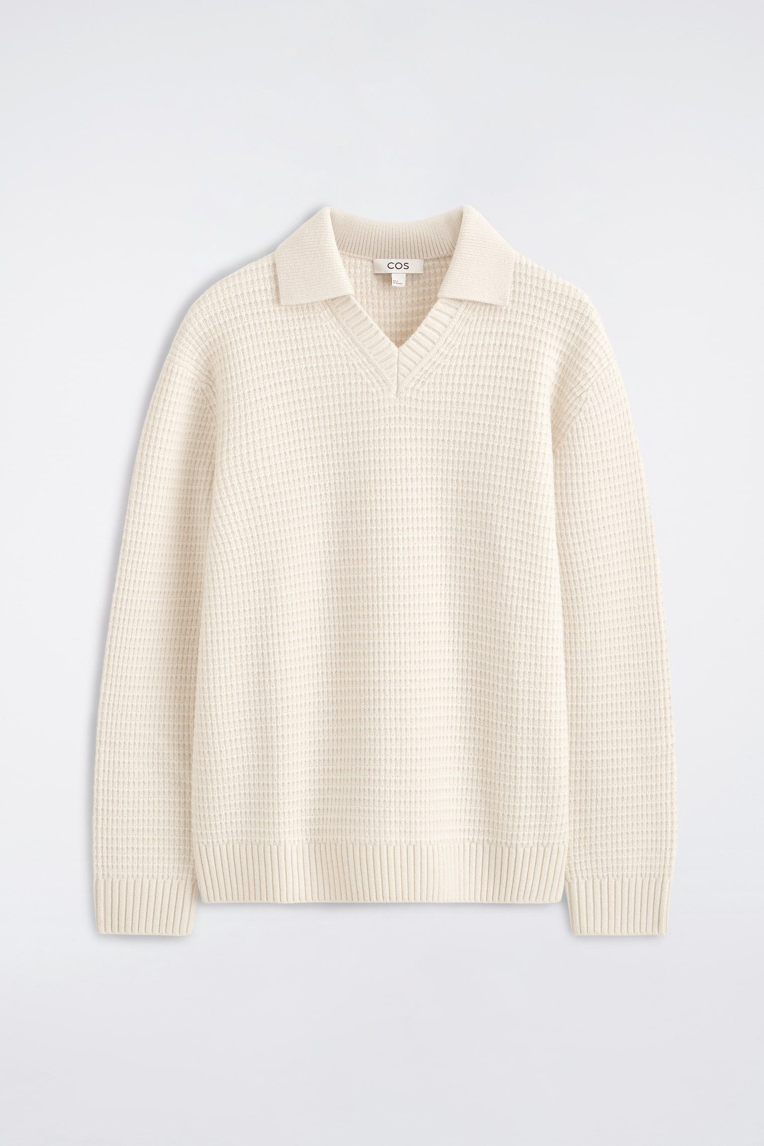 Un pull polo en laine à maille gaufrée, couleur crème, est présenté de face, mettant en valeur son motif texturé à maille gaufrée. Ce vêtement à manches longues présente un col polo ouvert avec un col en V sans boutons, des poignets côtelés et un ourlet côtelé. - 1