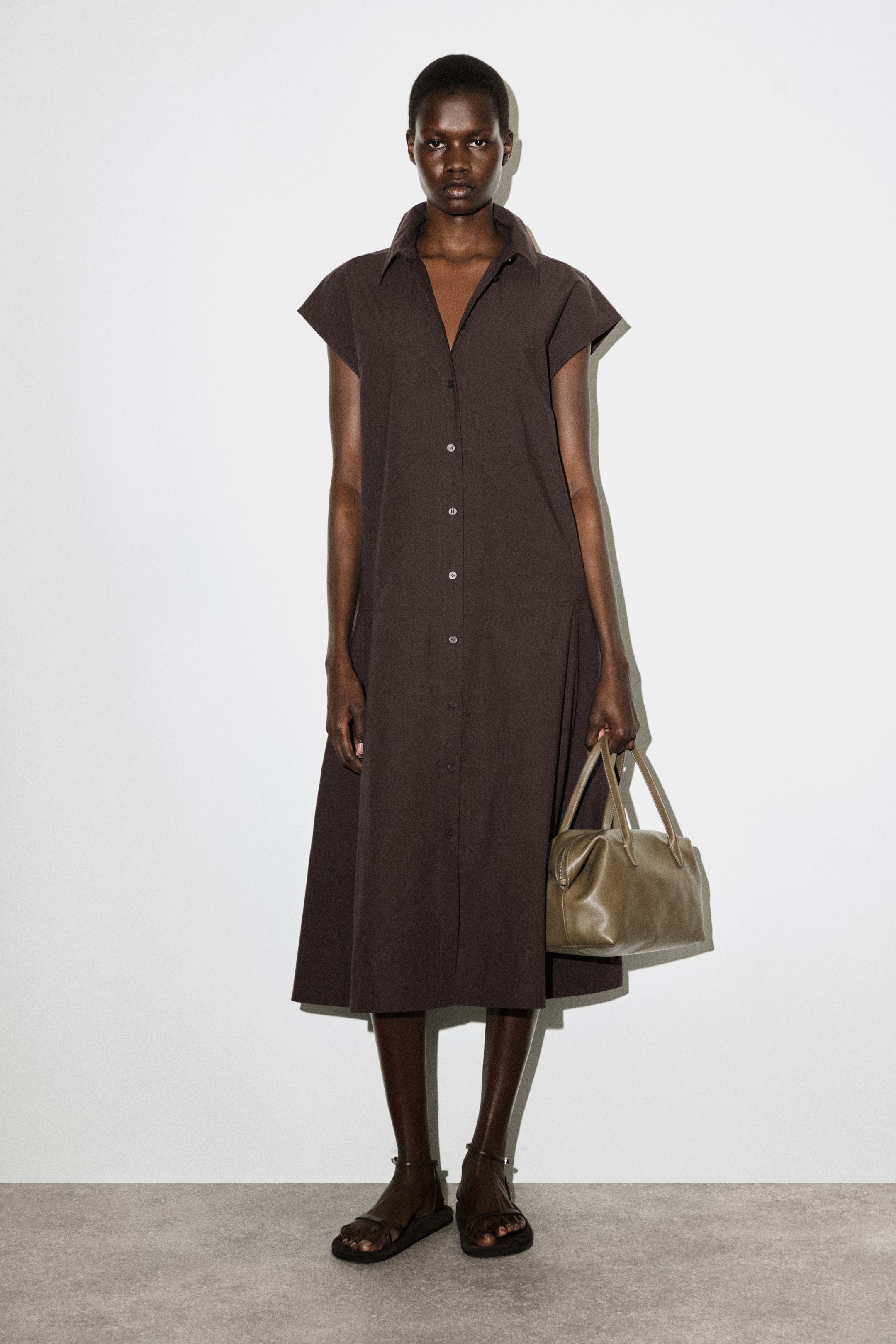 Agrandir l'image: Une robe-chemise midi marron foncé présente un col pointu et des manches courtes et larges. Elle est dotée d'une patte de boutonnage complète à l'avant avec des boutons de couleur claire et une silhouette en ligne A, tombant sous les genoux.