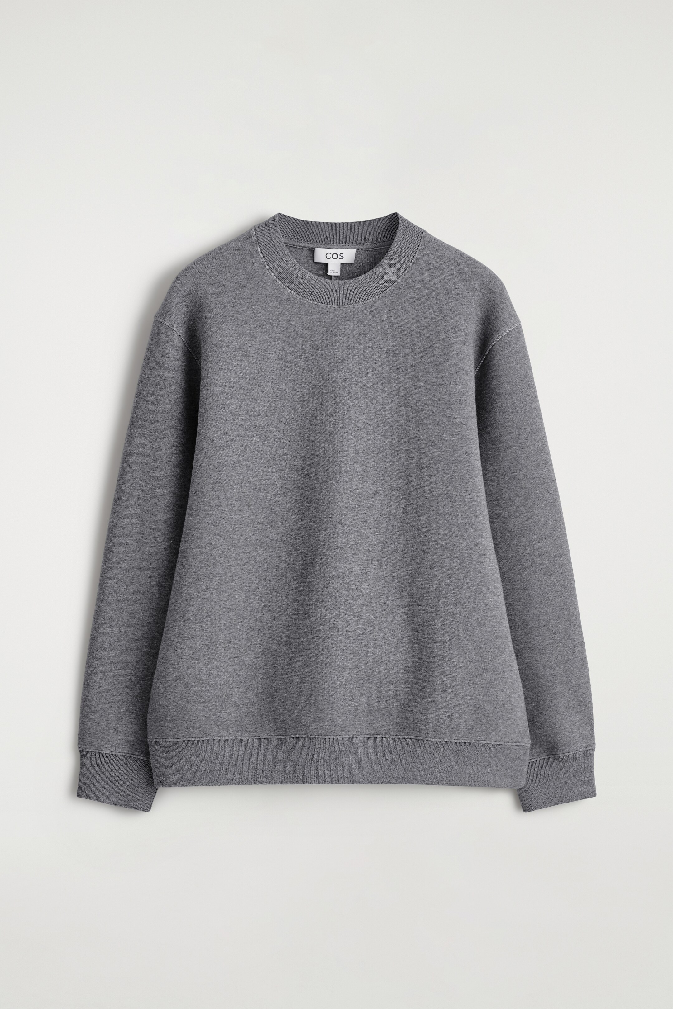 Ver imagem maior: Uma sweatshirt cinzenta é mostrada de FRENTE, apresentando um corte descontraído, uma gola redonda e acabamentos finamente canelados na gola, punhos e bainha. O tecido suave e ligeiramente estruturado exibe costuras visíveis em torno da gola e das cavas.