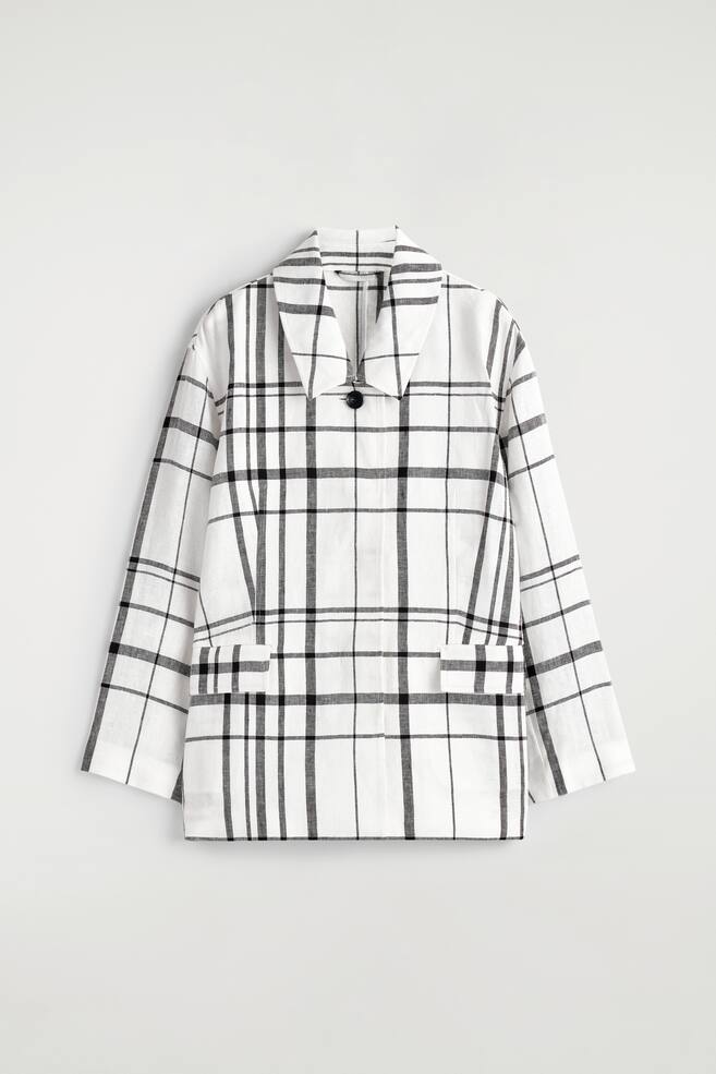 Eine weiße Karojacke präsentiert ihre VORDERSEITE mit schwarzen, sich kreuzenden Linien, die das Muster bilden. Sie ist mit einem Umlegekragen gestaltet, der einen V-Ausschnitt bildet, einem einzelnen schwarzen Knopfverschluss und zwei aufgesetzten Taschen auf der unteren Vorderseite, mit langen Ärmeln. - 1