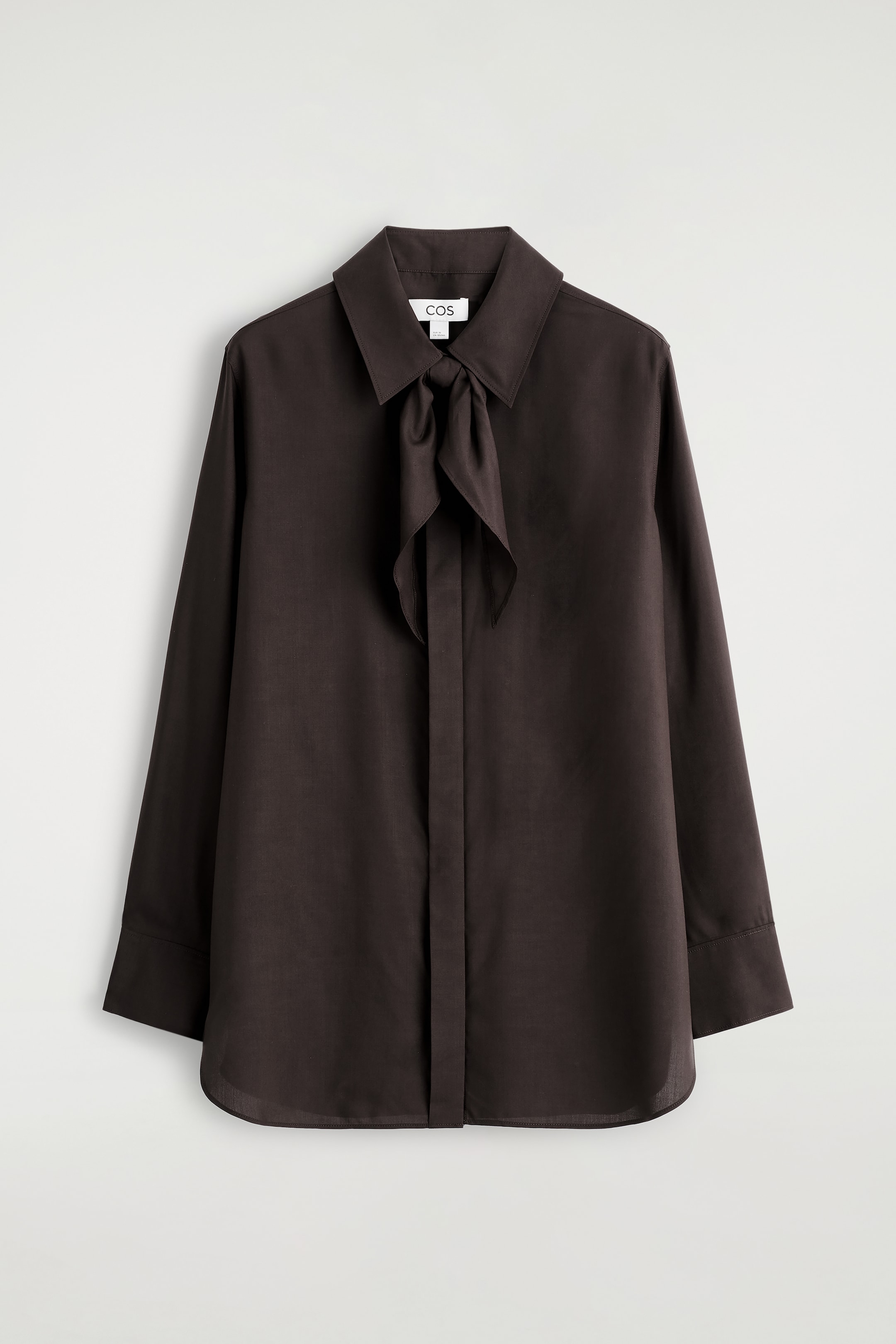 Ver imagen más grande: Una camisa de mujer se presenta FRENTE en un rico color castaño, confeccionada con lujosa seda de morera. Presenta un cuello clásico y una bufanda tonal que forma un nudo suelto en el escote. Una tapeta de botones oculta recorre la parte delantera, y las mangas largas terminan en puños anchos, mientras que el dobladillo es sutilmente redondeado.
