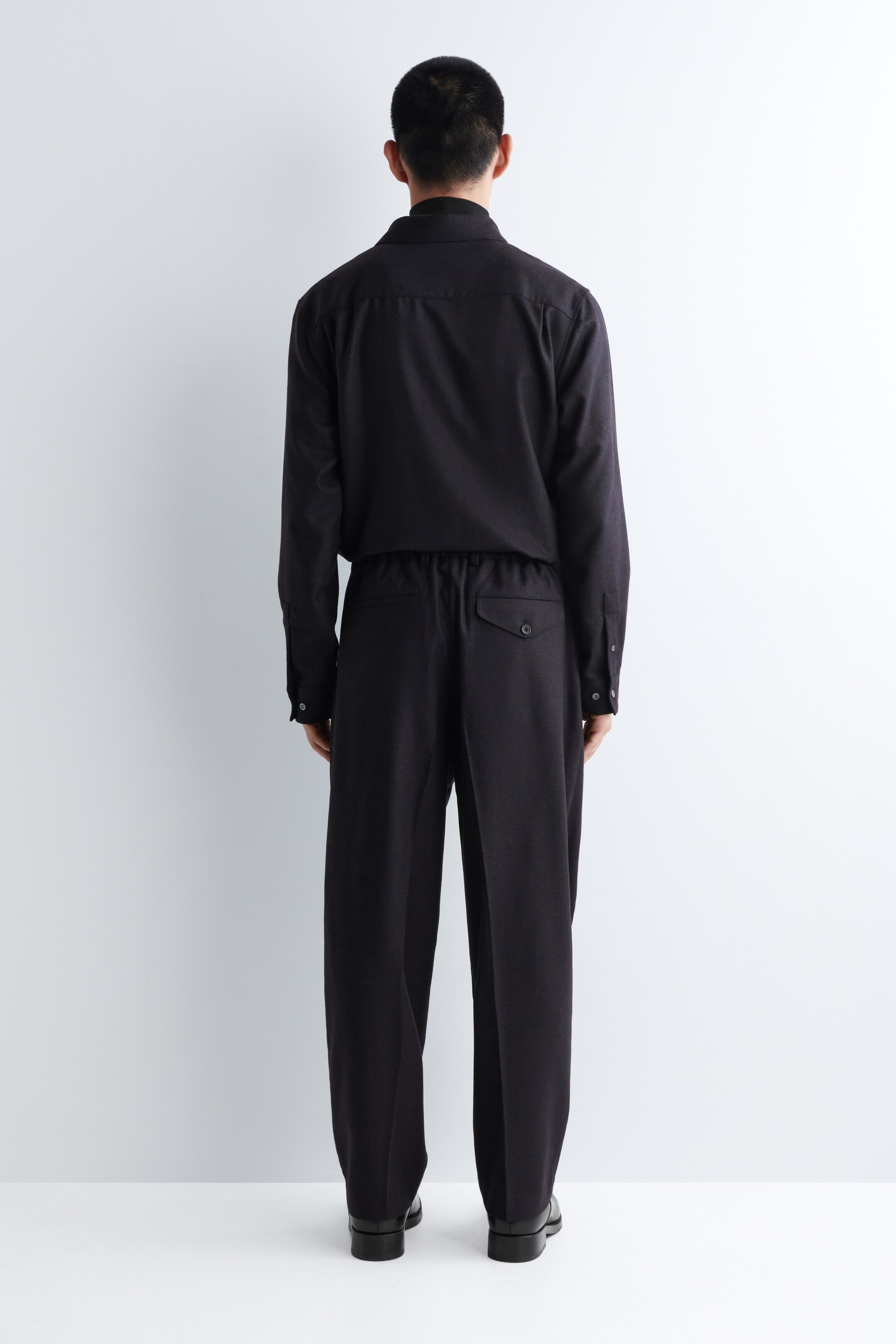 Agrandir l'image: Une chemise à col foncé et finement texturée ainsi qu'un pantalon assorti sont portés, vus de dos. La chemise à manches longues est rentrée dans le pantalon, qui dispose d'une taille élastiquée et d'une poche arrière à rabat boutonnée.