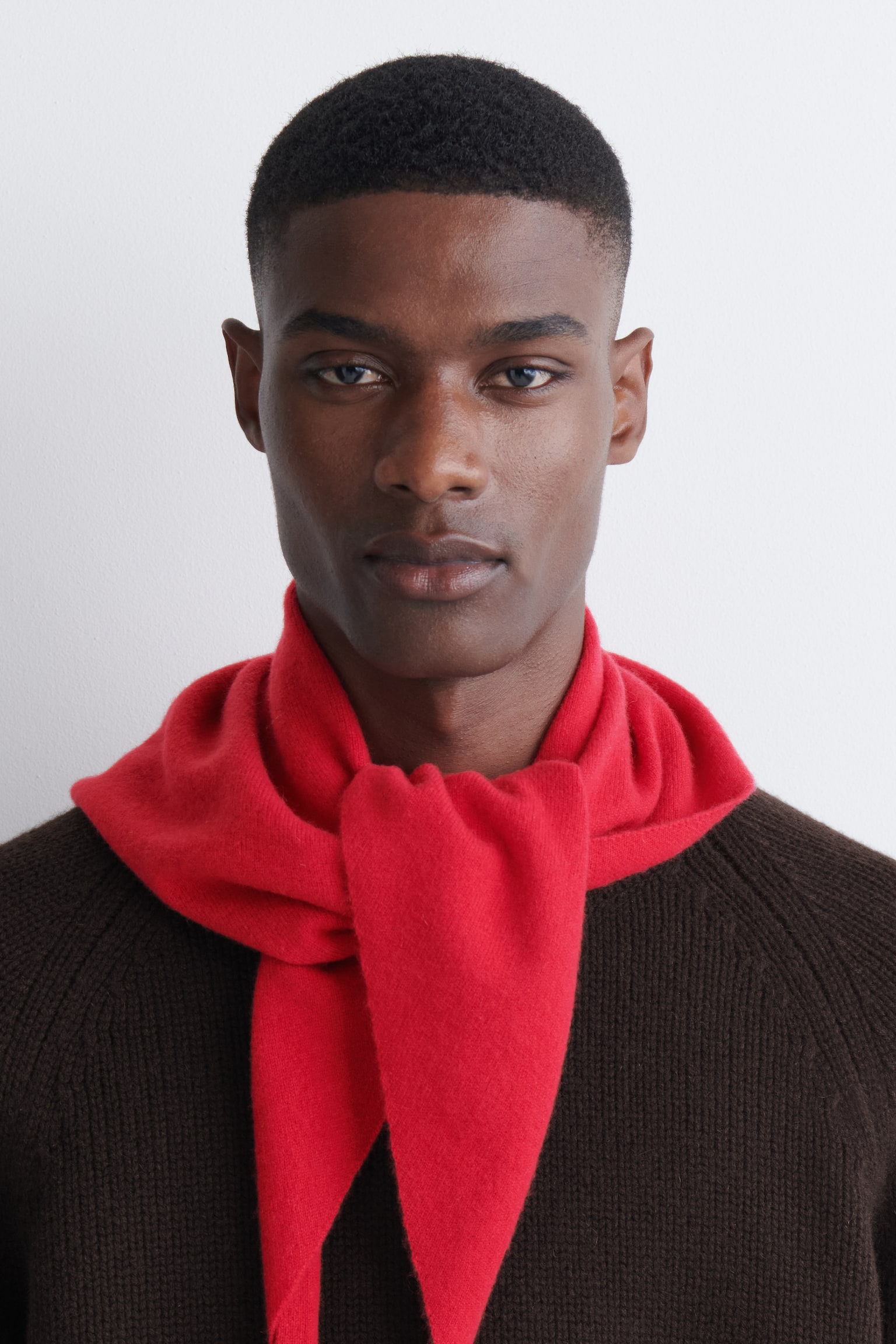 Un foulard triangle rouge est posé à plat, plié avec ses extrémités croisées sur le devant, créant un effet superposé qui se rétrécit jusqu'à un point central. Le tissu en cachemire affiche une texture douce et finement tricotée. - 1