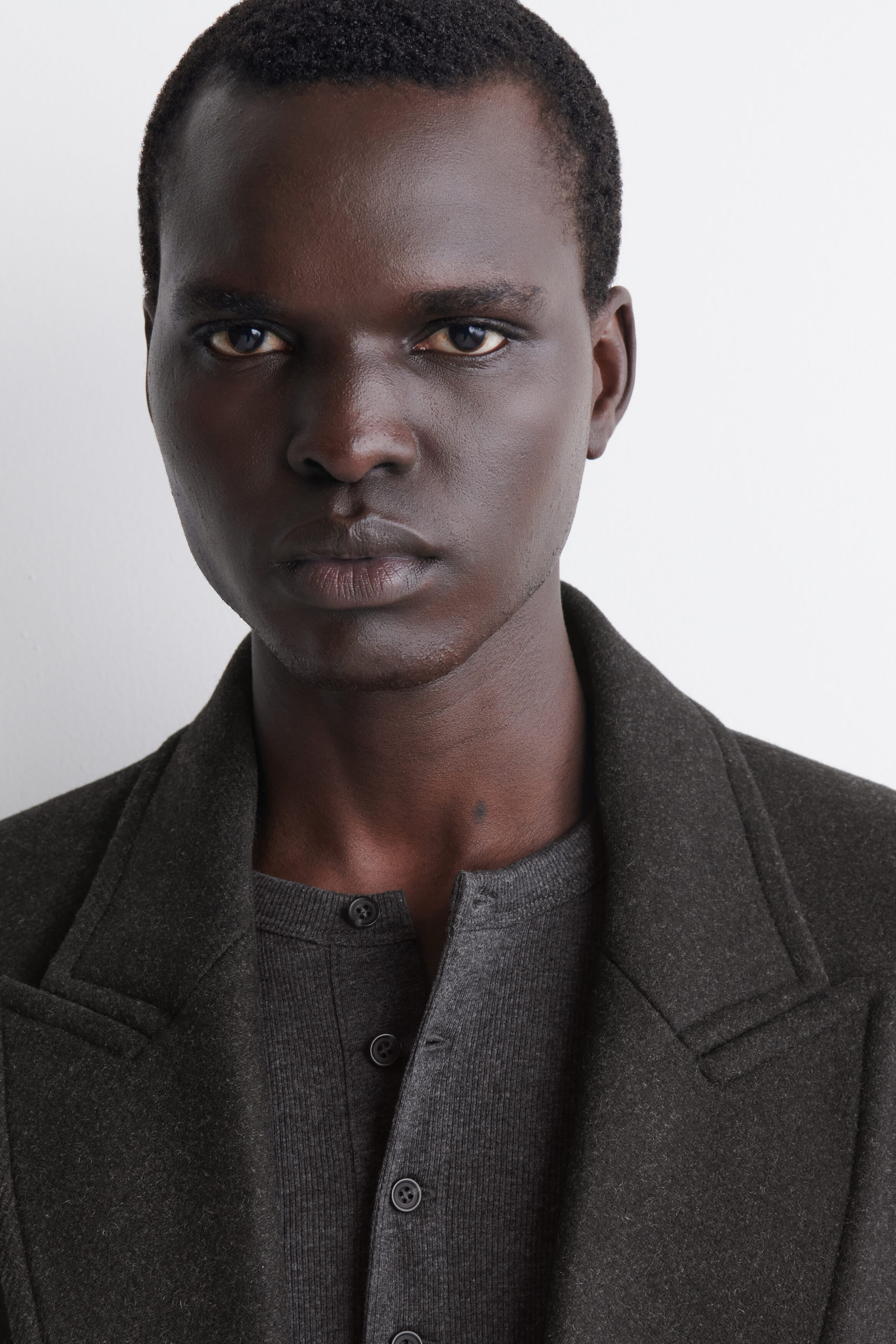 The slim ribbed cotton long-sleeve Henley T-shirt is worn as a base layer under a dark, structured coat with wide notch lapels. It features a fine ribbed texture and a partially unbuttoned front placket with dark buttons. The slim ribbed cotton long-sleeve Henley T-shirt is worn as a base layer under a dark, structured coat with wide notch lapels. It features a fine ribbed texture and a partially unbuttoned front placket with dark buttons.
