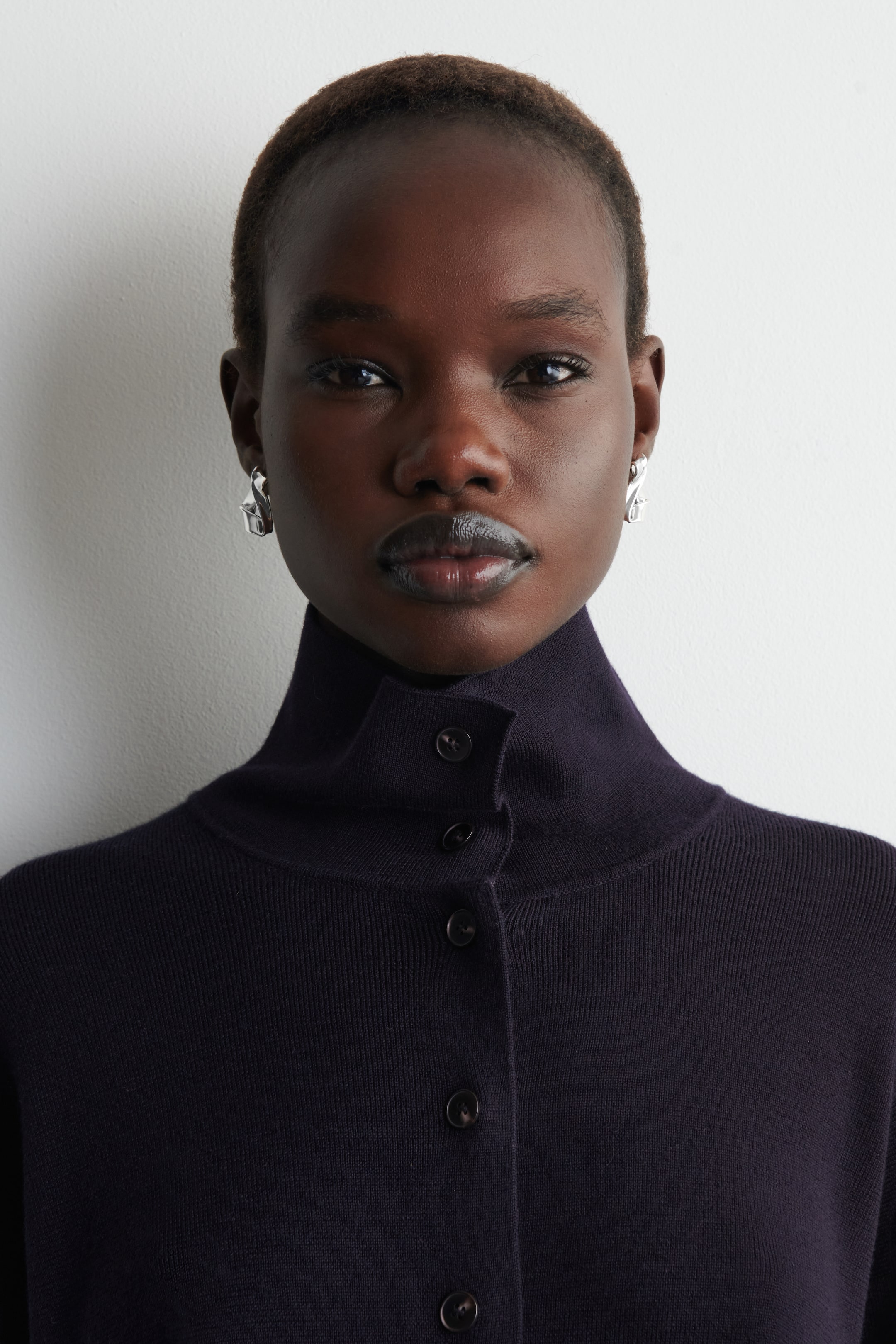 View larger image: A dark knit top featuring a ribbed mock neck collar and a front button placket with dark, round buttons, presenting its front and upper right side.