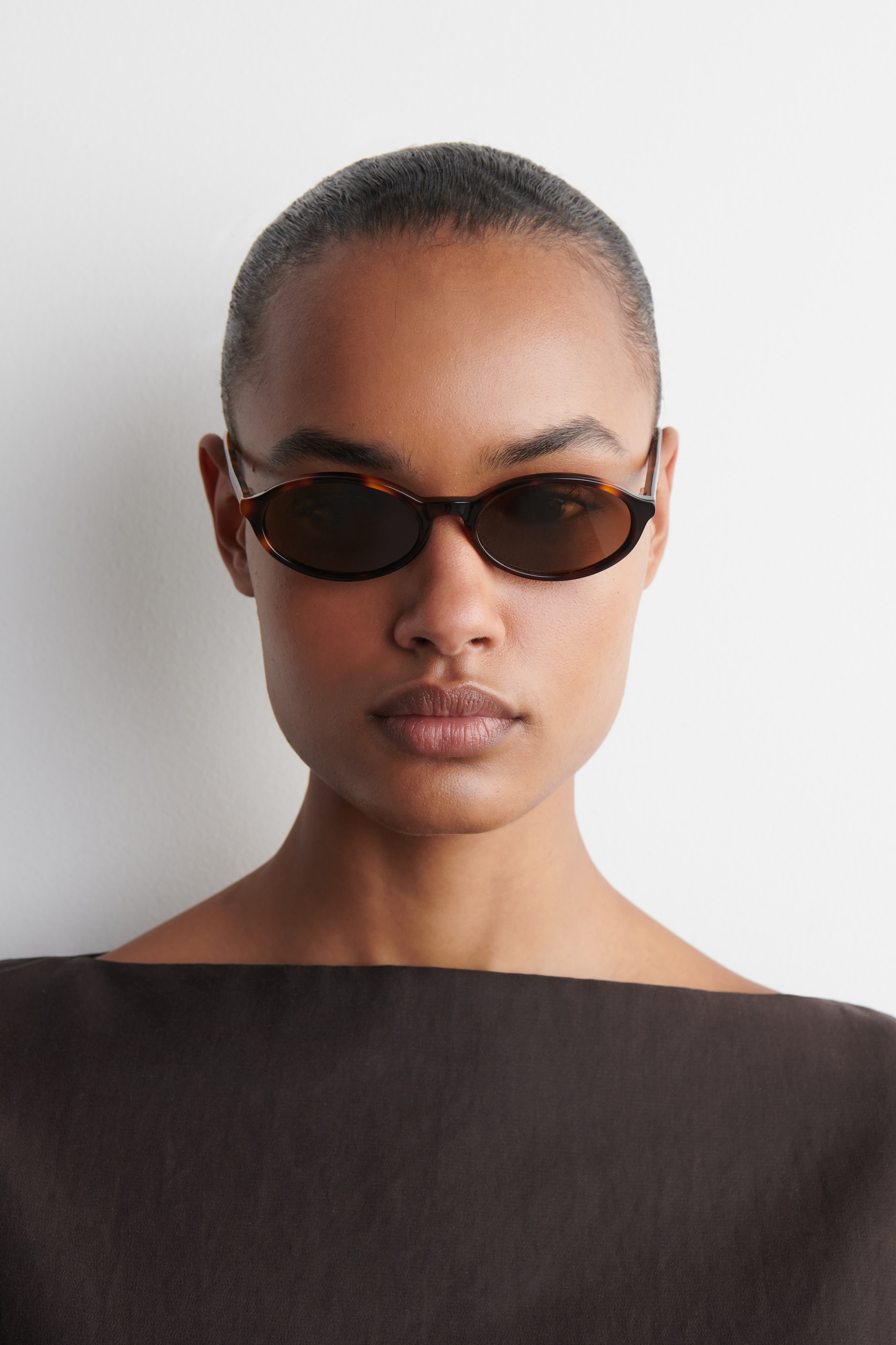 Größeres Bild anzeigen: Die Sonnenbrille zeigt schmale, ovale Gestelle in Schildpattoptik mit dunklen, getönten Gläsern und wird frontal von einer Person getragen, um die Passform zu demonstrieren.