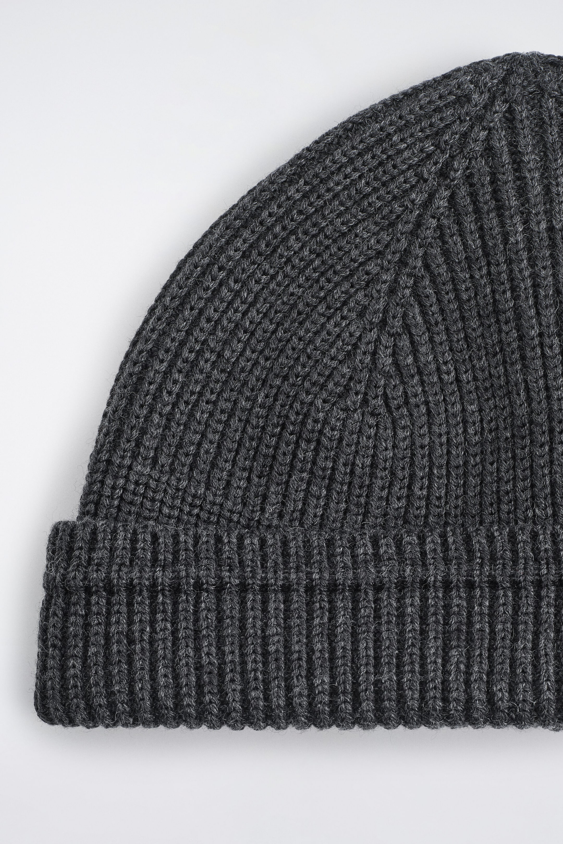 A dark gray ribbed wool-cotton fisherman beanie is shown in a close-up front view, highlighting its thick, textured rib-knit pattern and folded cuff.
