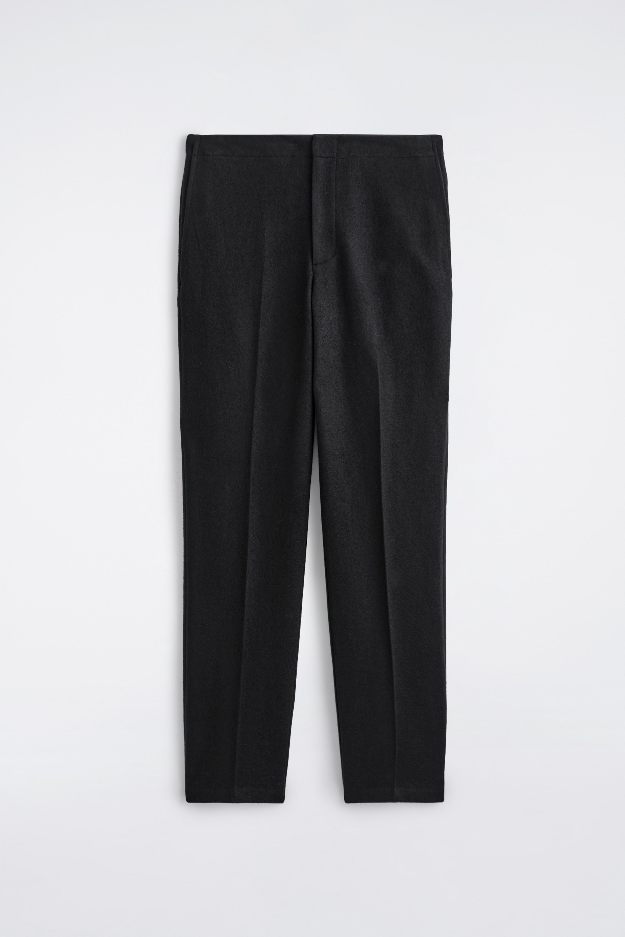 Agrandir l'image: PANTALONS EN LAINE BOUILLIE ÉLASTIQUES sont présentés de face, affichant une finition mate et sombre. Ils présentent une ceinture plate et ajustée avec une fermeture à glissière dissimulée. Des plis marqués descendent au centre de chaque jambe droite, se terminant par un ourlet net et non retourné.