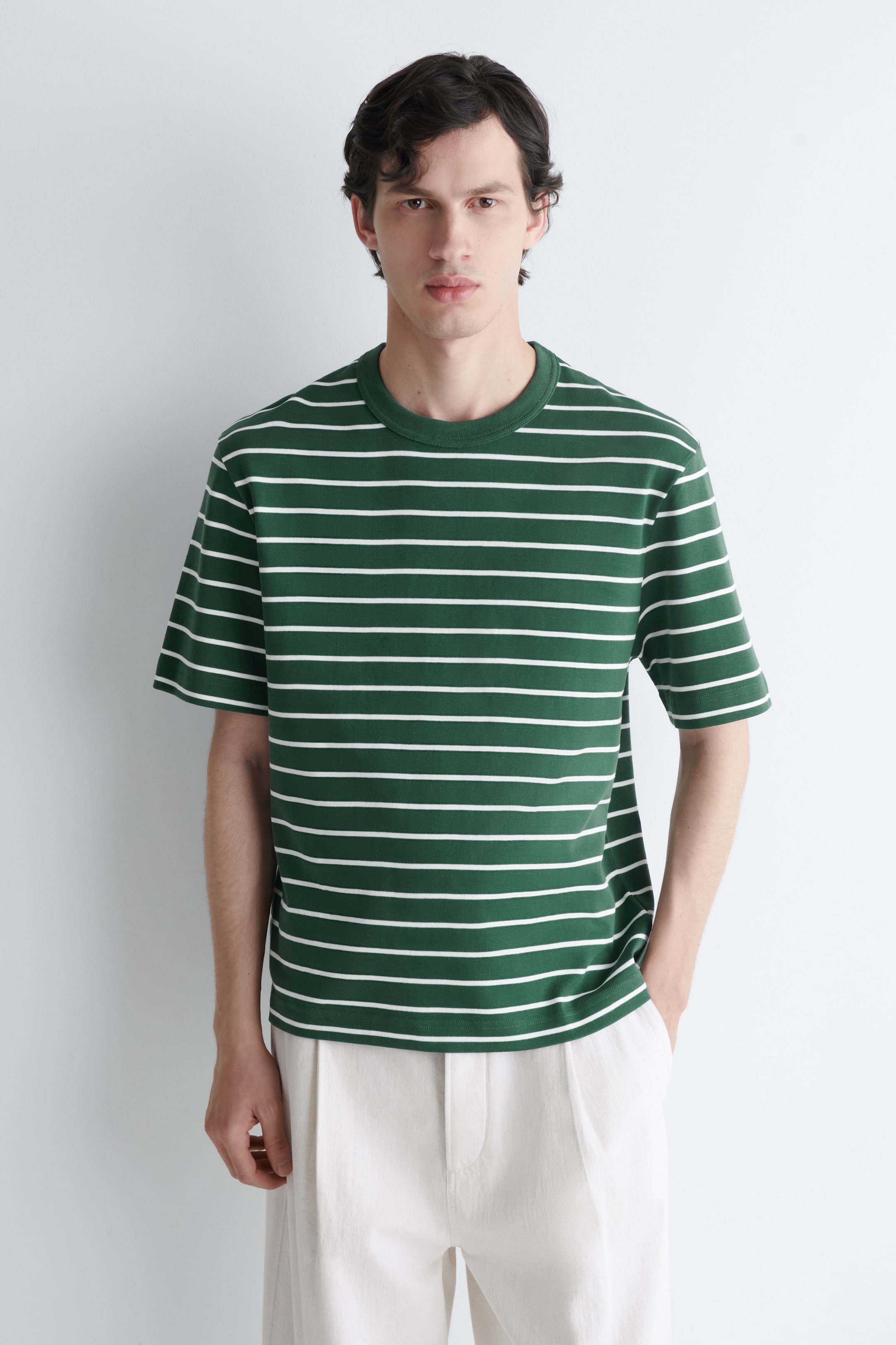 Visa större bild: En grön t-shirt med vita horisontella ränder bärs i en vanlig passform, med en ribbad rund halsringning och korta ärmar.