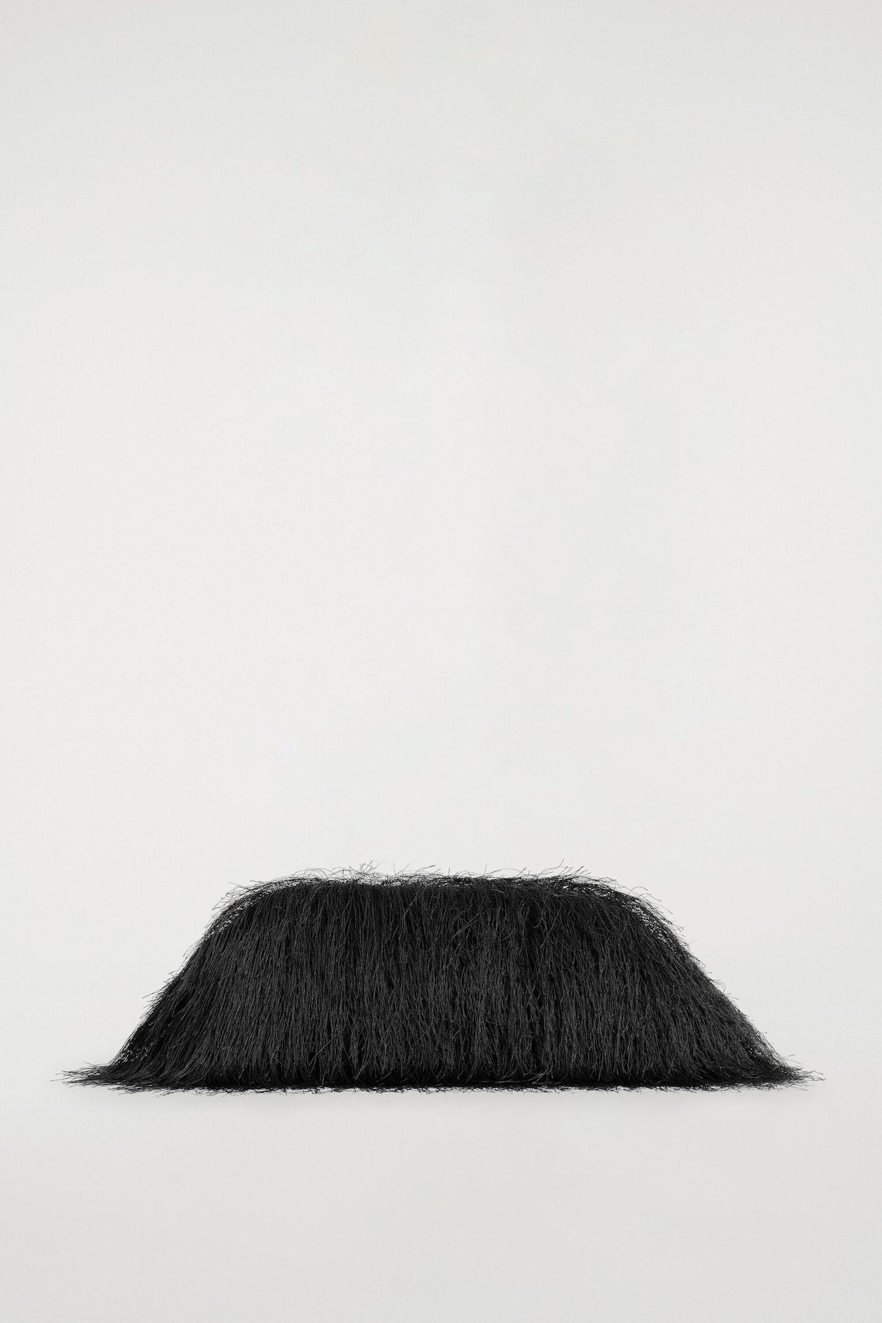 A black fringed clutch bag is resting flat in a front-facing view, showcasing a structured, dome-like shape. The bag features long, fine, dense black fringe draping downward to completely obscure the underlying frame.