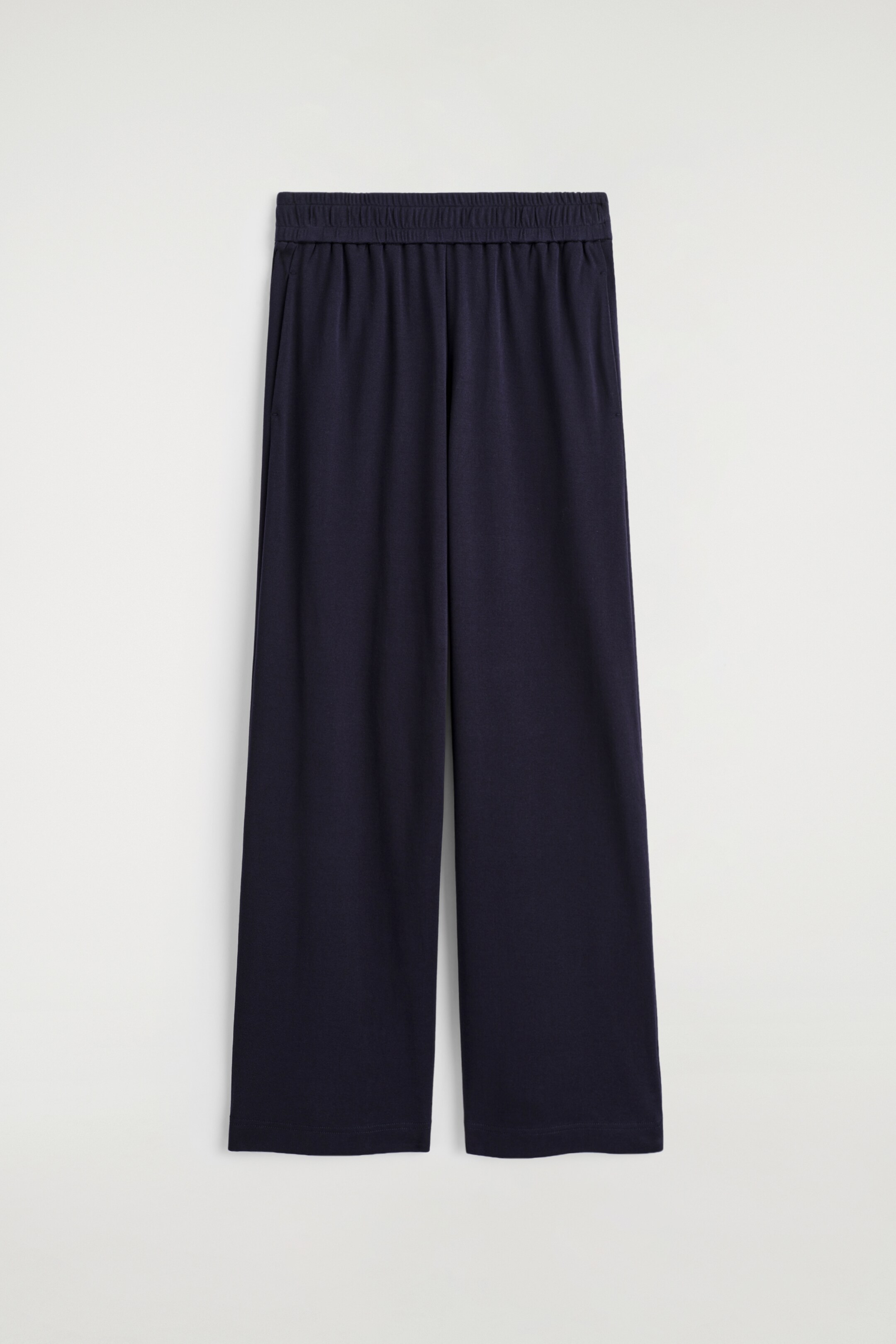 Agrandir l'image: Les FLUID JERSEY JOGGERS sont orientés vers l'avant, apparaissant dans une couleur bleu foncé. Ils présentent une silhouette à jambes larges avec une taille élastiquée montrant un froncement visible, et sont finis avec des poches latérales discrètes et un ourlet droit.