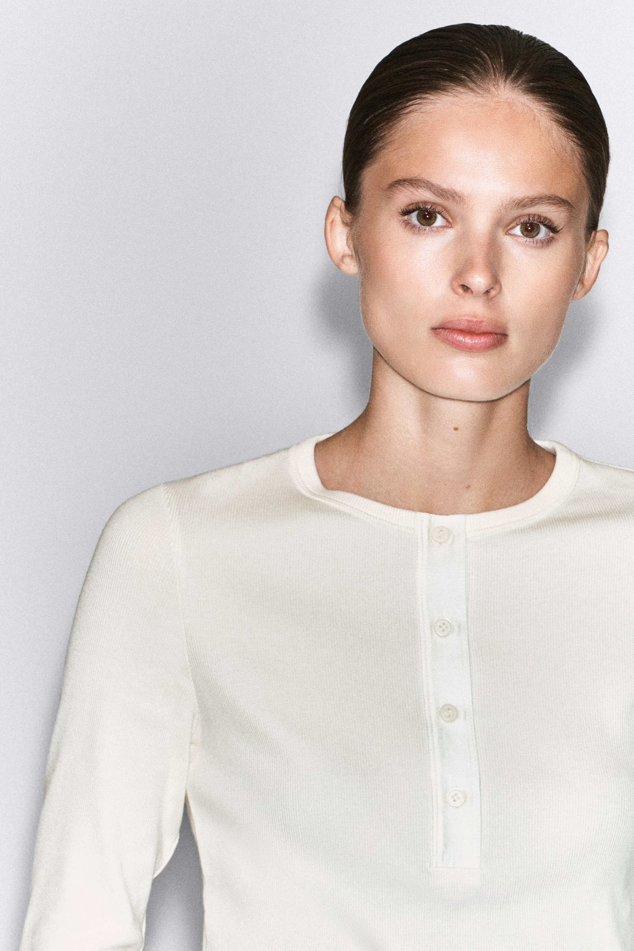 A ribbed cotton henley top in off-white is being worn by the model, featuring a crew neckline and a buttoned half-placket. A ribbed cotton henley top in off-white is being worn by the model, featuring a crew neckline and a buttoned half-placket.