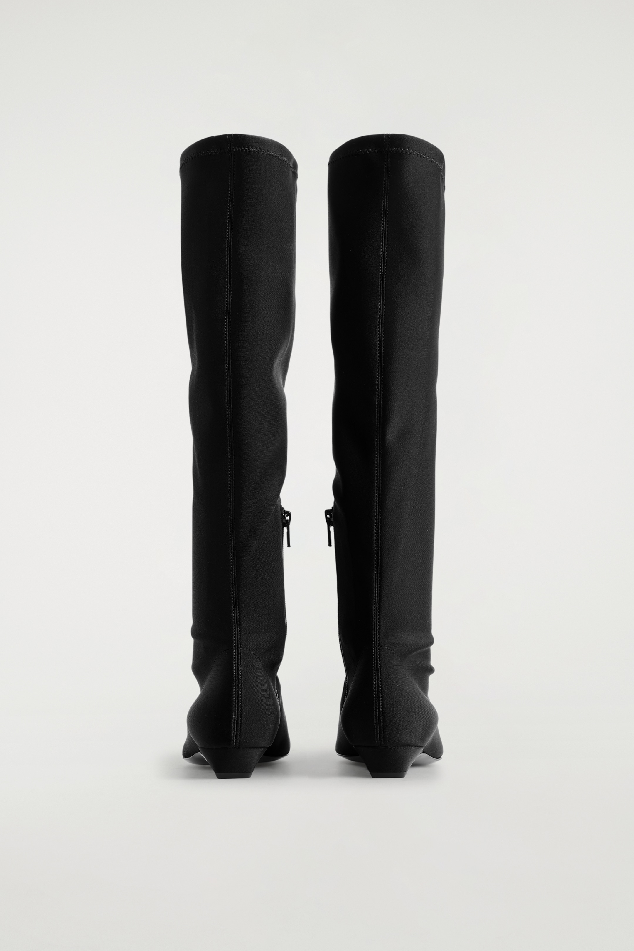 View larger image: BACK view of black Pointed Scuba Knee Sock Boots, featuring a smooth, stretchy texture. Each boot is showing a vertical seam running up the back of its shaft, a visible zipper closure on the inner side extending from the ankle, and is resting on a low, matching block heel.