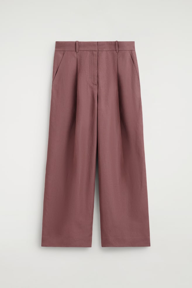 Los pantalones en color rosa empolvado se muestran desde el frente, presentando un diseño de talle alto con trabillas para cinturón, bolsillos laterales inclinados y pliegues prominentes en la parte delantera. Los pantalones presentan piernas anchas que se extienden rectas hasta dobladillos de largo completo. - 1