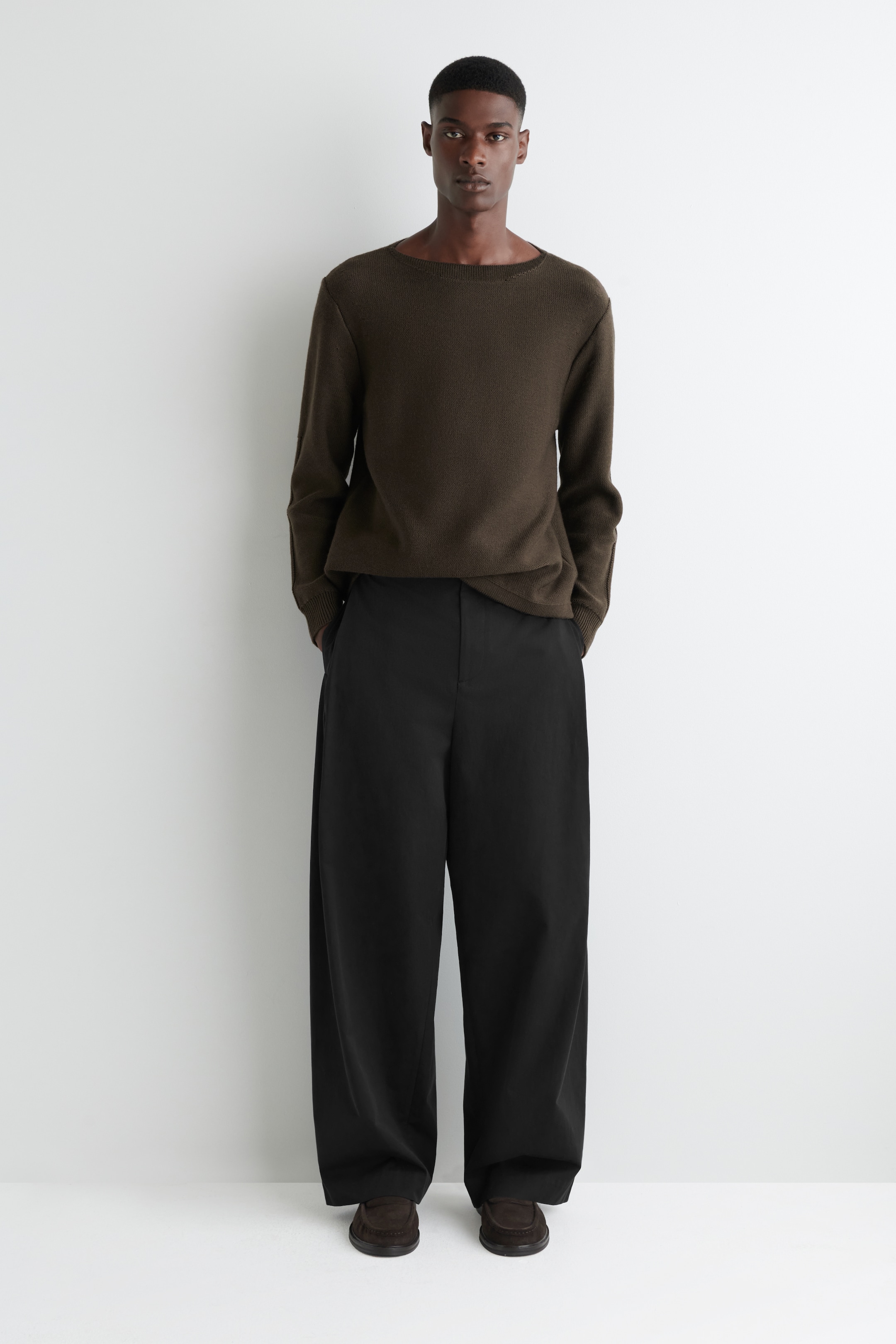 Agrandir l'image: Un haut à manches longues vert olive foncé avec un col bateau est porté, présenté de face. Il est assorti à un pantalon noir à jambes larges et des mocassins marron foncé.
