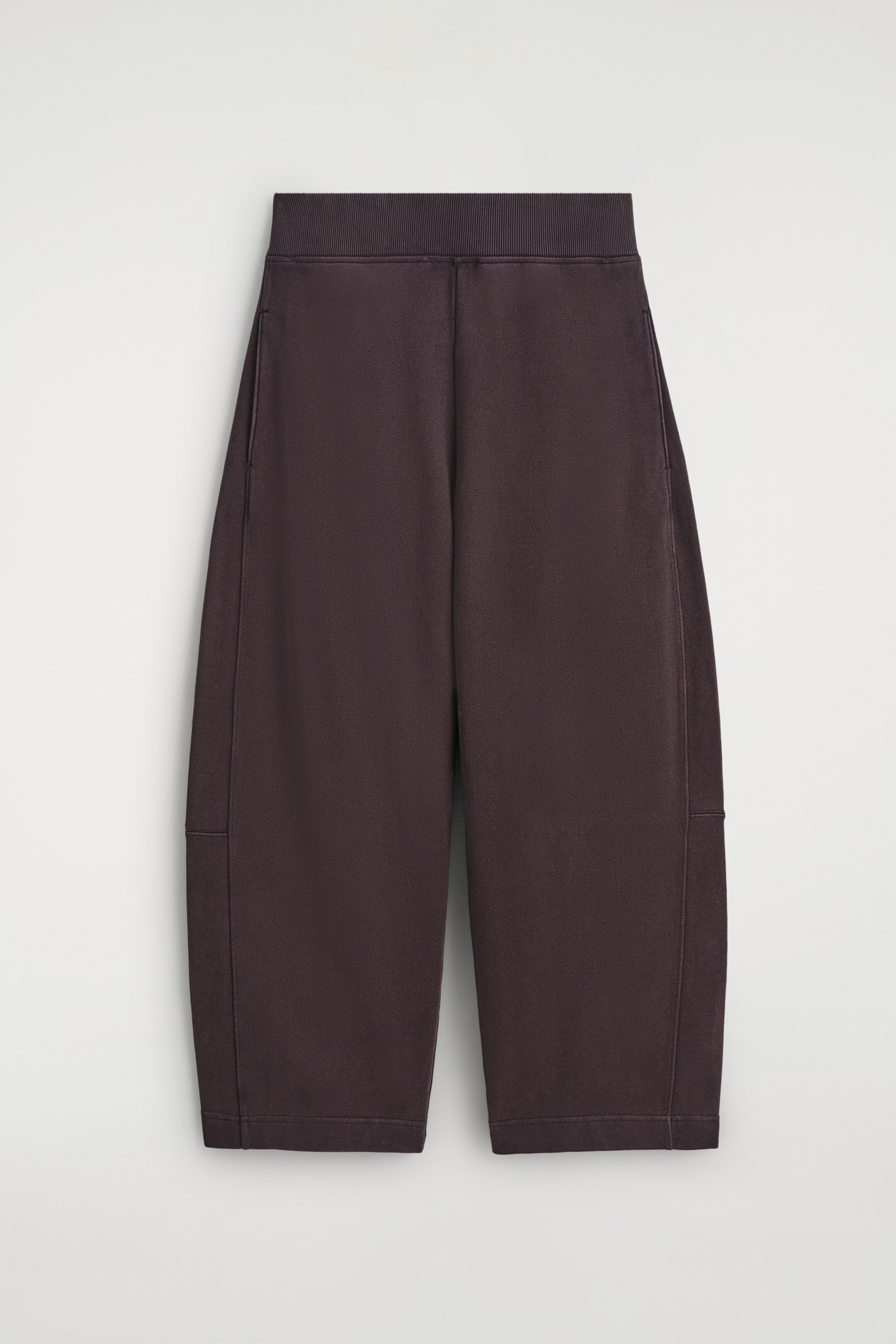 View larger image: Front view of dark brown joggers, featuring a wide, ribbed elasticated waistband and a relaxed, cropped fit. Visible seam detailing is running along the sides, with horizontal stitching appearing near the mid-calf.