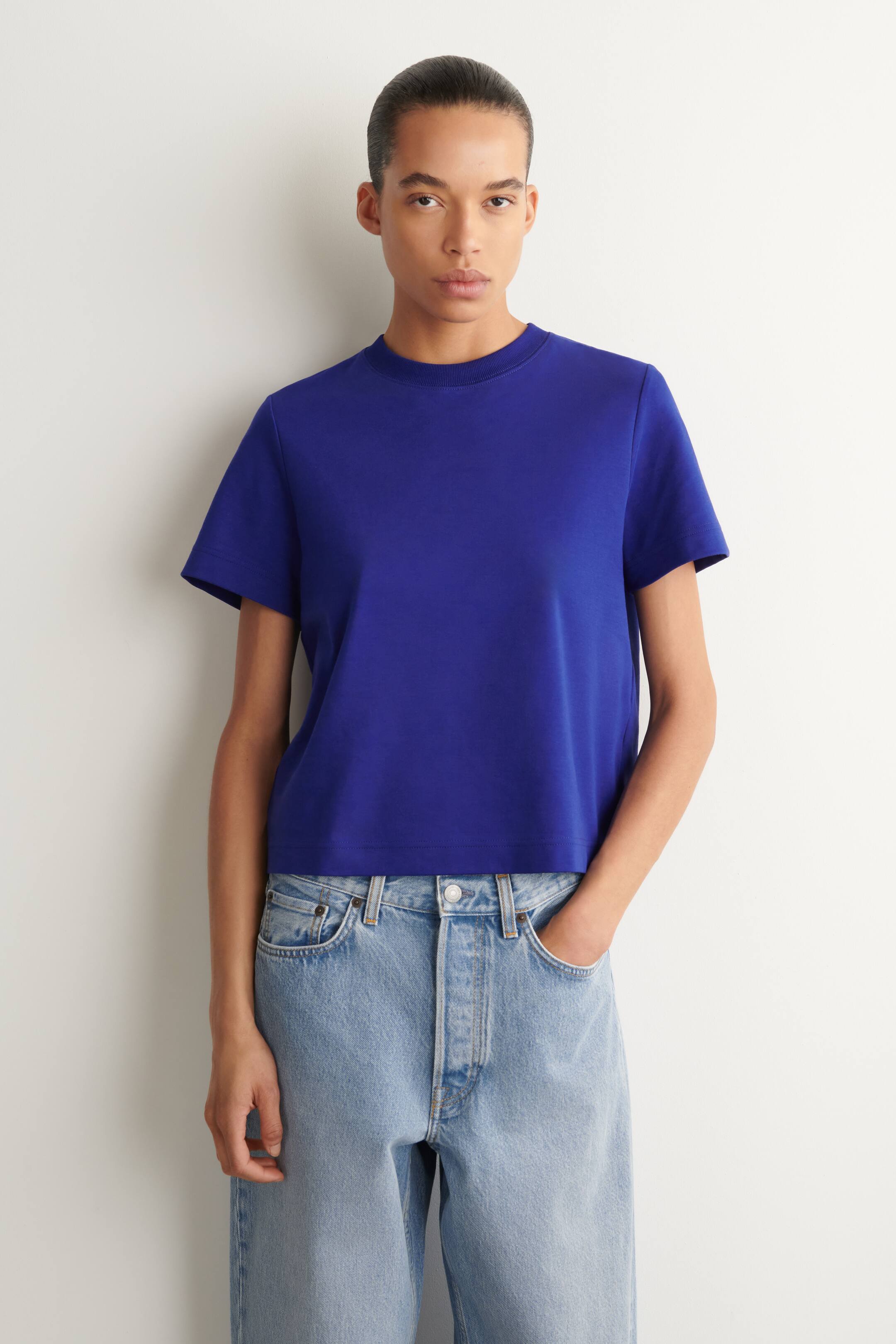 View larger image: A royal blue T-shirt is being worn, featuring a crew neck, short sleeves, and a cropped hemline that ends just above light-wash jeans.