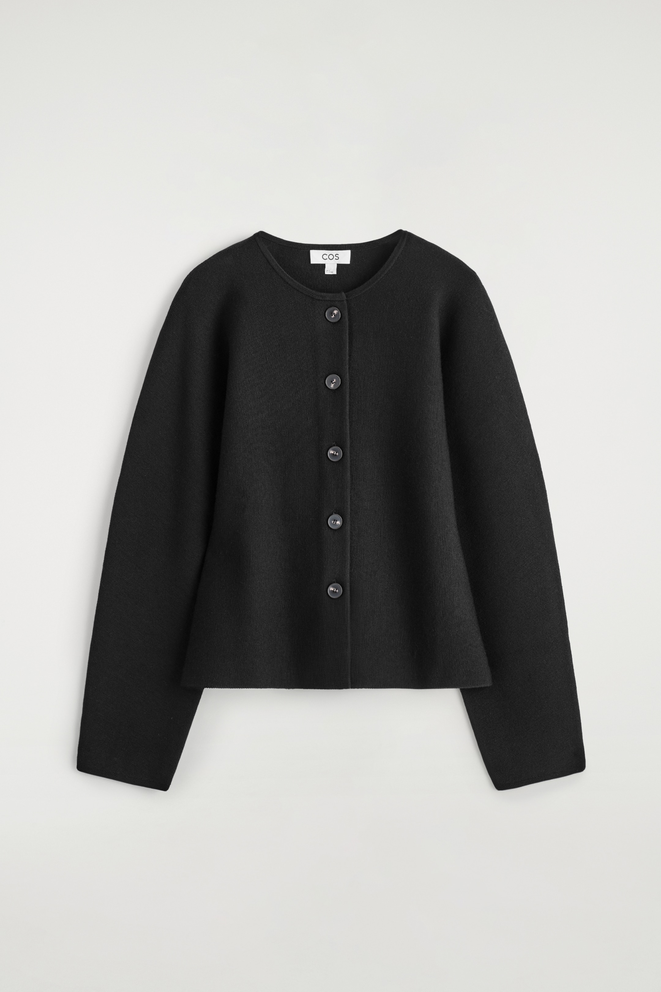 Agrandir l'image: Un cardigan noir est présenté de face, avec un col rond et une fermeture complète à boutons avec cinq boutons circulaires foncés. Il présente des manches longues et un ourlet structuré, légèrement évasé, créant une silhouette sculpturale.