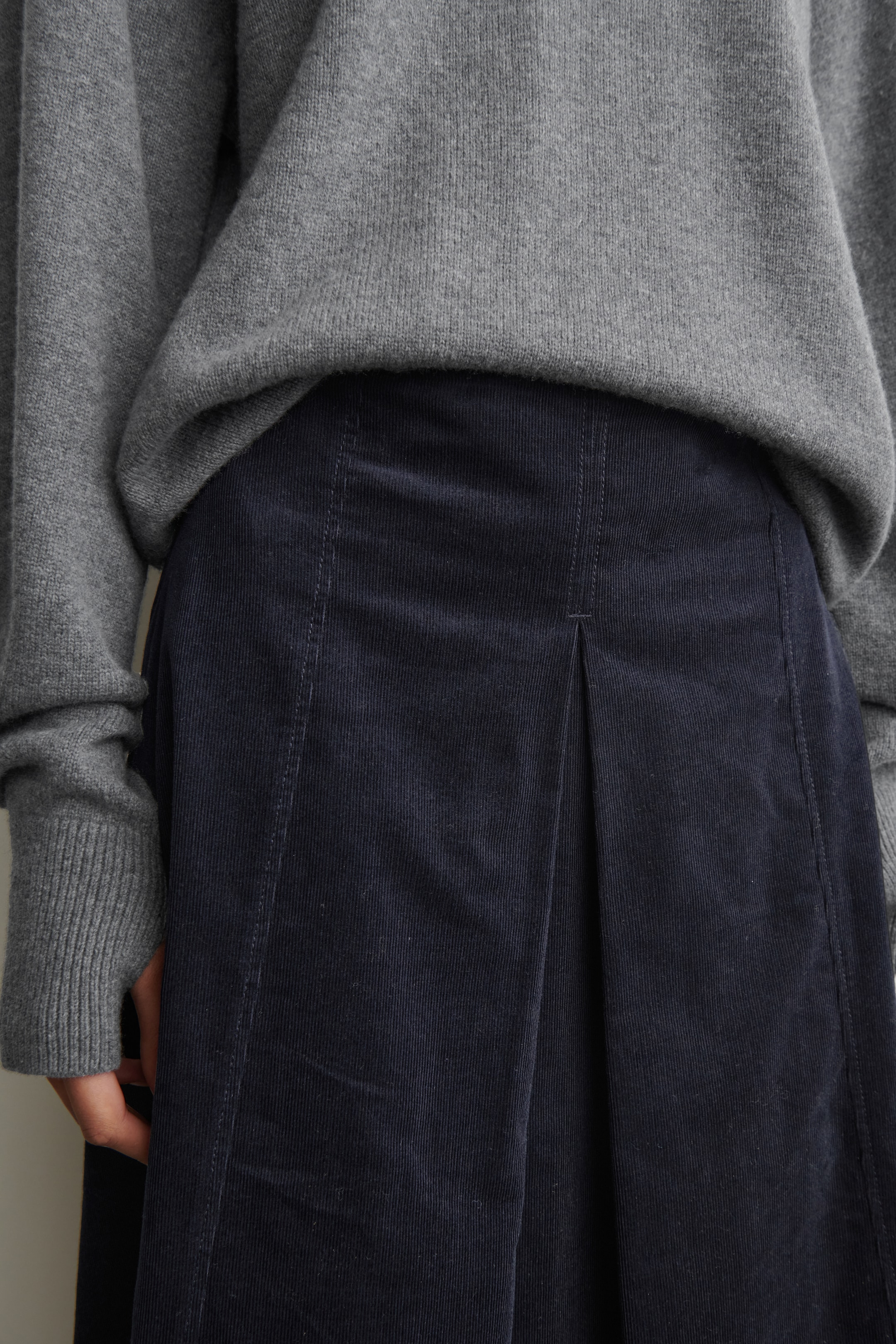Agrandir l'image: Un pull gris en tricot avec des poignets côtelés est superposé à une jupe en velours côtelé bleu marine, les deux présentés de face. La jupe affiche des côtes en velours côtelé verticales, des coutures verticales et un pli central à la taille.